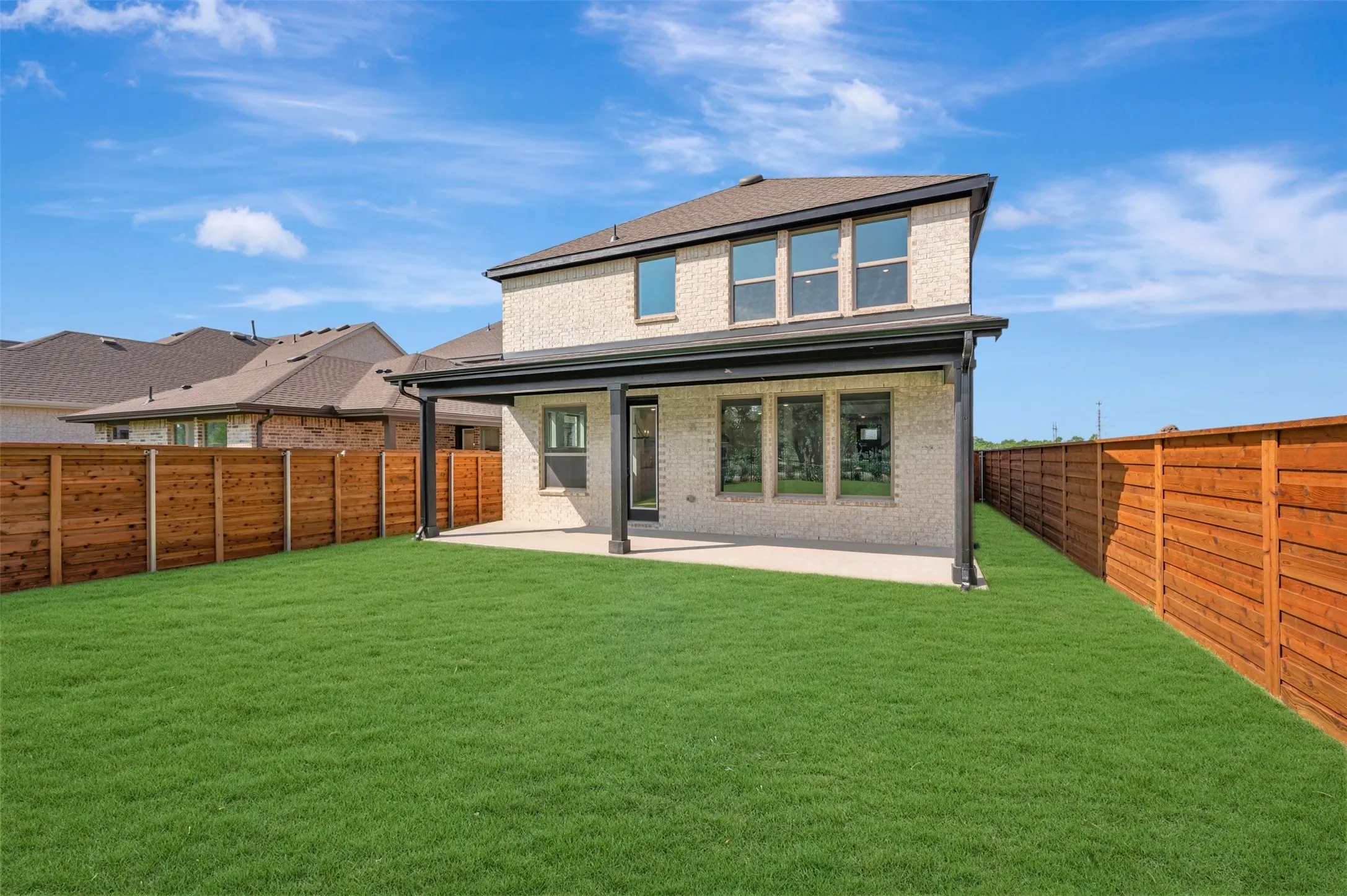 Expansive backyard with a manicured lawn, a full wooden privacy fence, and a covered patio with dark support pillars