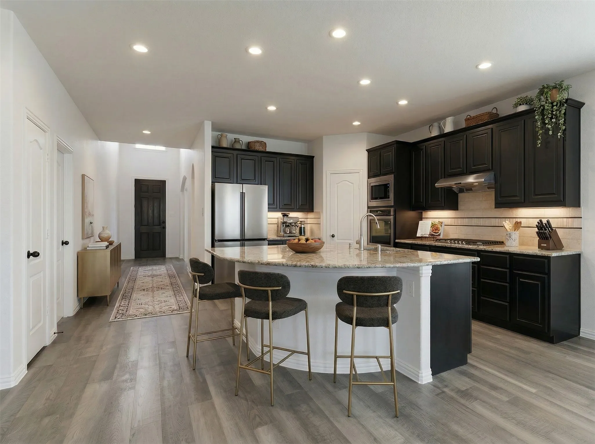 Kitchen with dark cabinets, light stone countertops, an island with sink, and recessed lighting