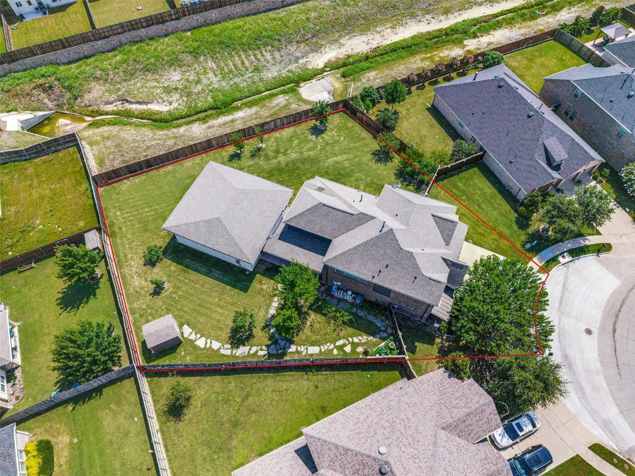 Expansive property featuring a large main residence with a gabled roof, an auxiliary structure, a stone pathway, a substantial grassy yard, and mature trees