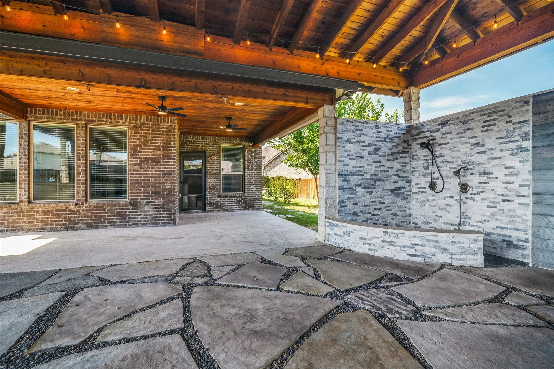 Covered patio featuring a flagstone and gravel inlay, exposed wood beam ceiling, and string lighting