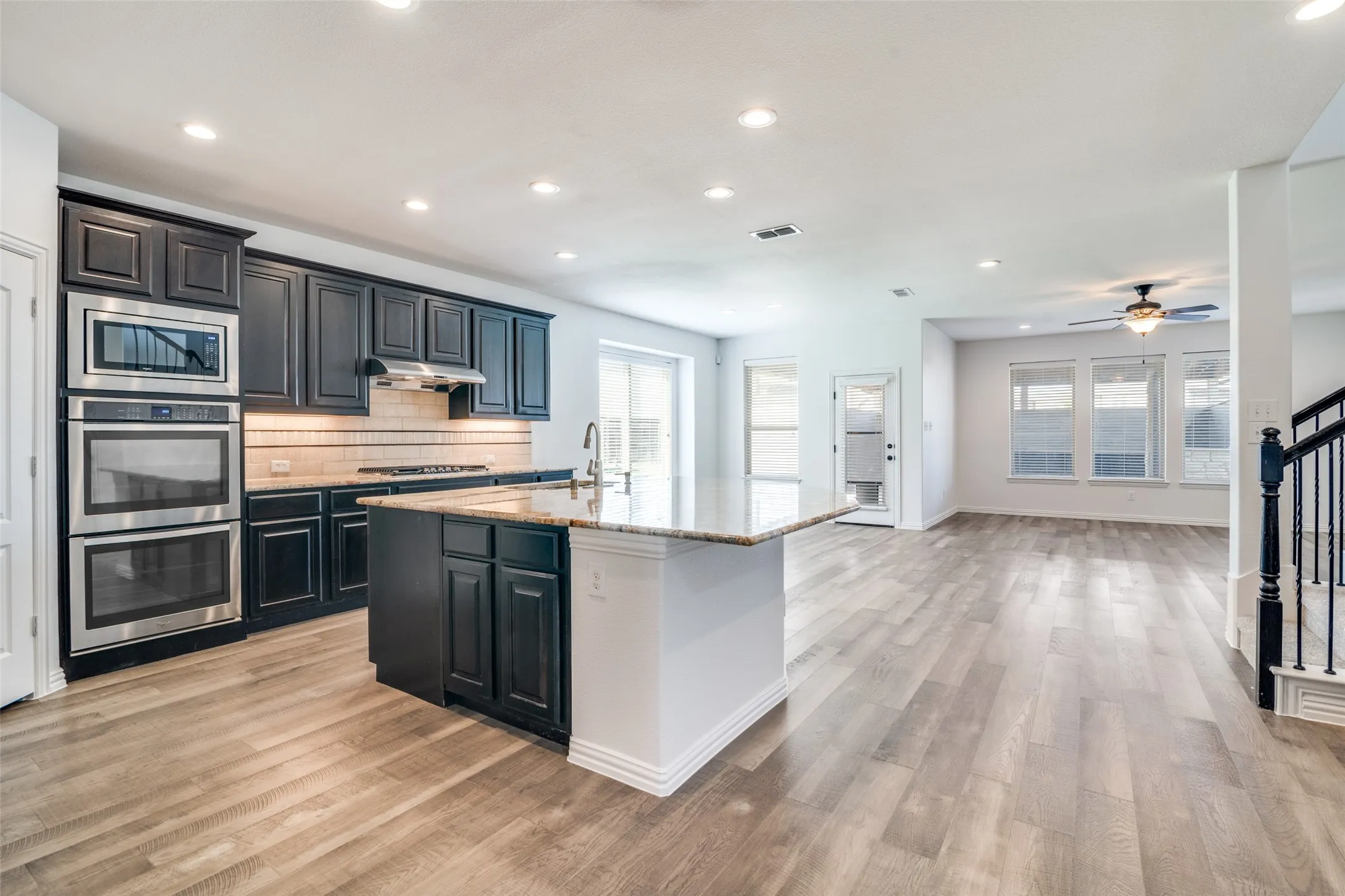 Kitchen featuring stainless steel appliances, light stone countertops, recessed lighting, light wood-style flooring, and a center island with sink
