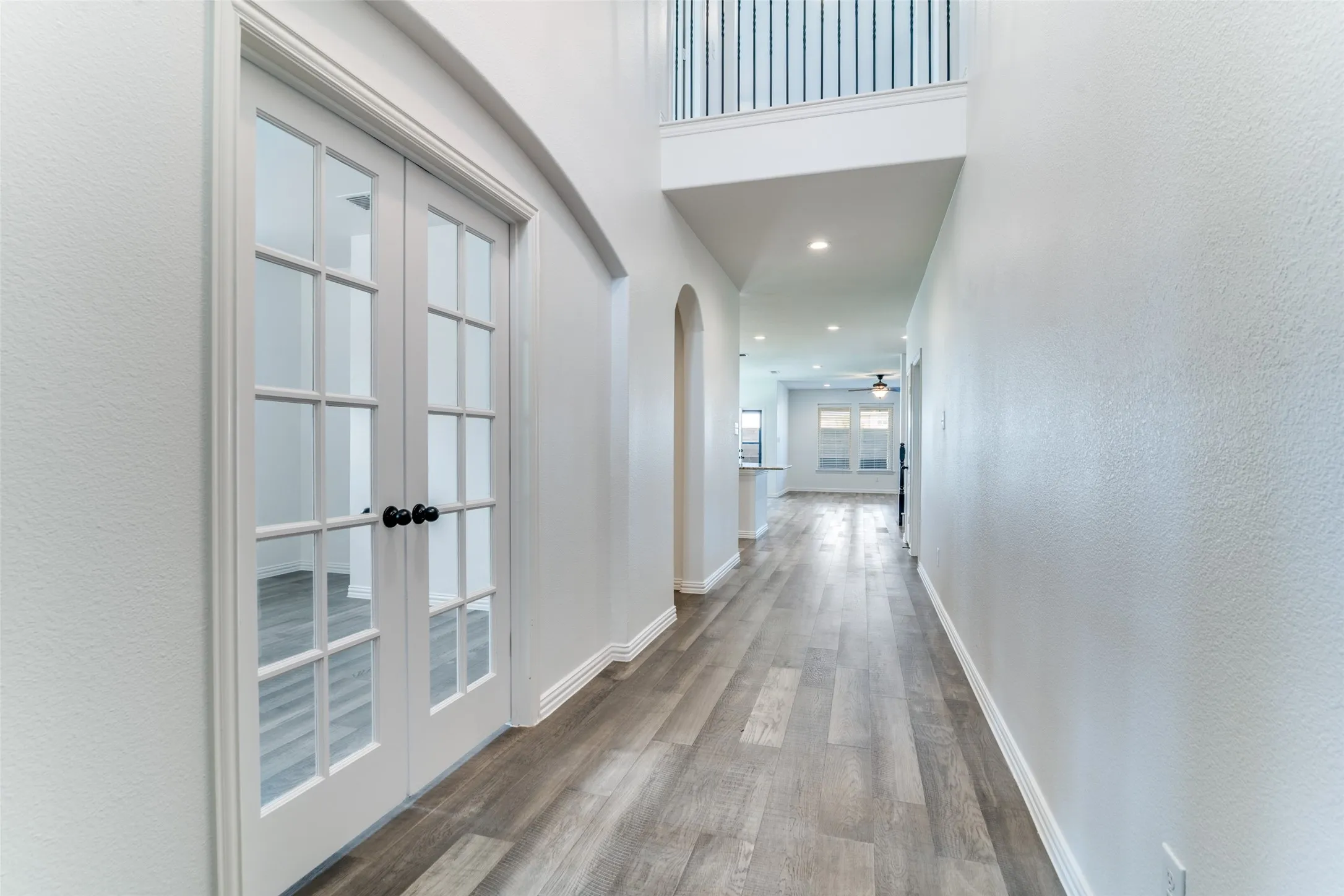 Hallway with light wood finished floors, arched walkways, a textured wall, recessed lighting, and french doors leading to the office
