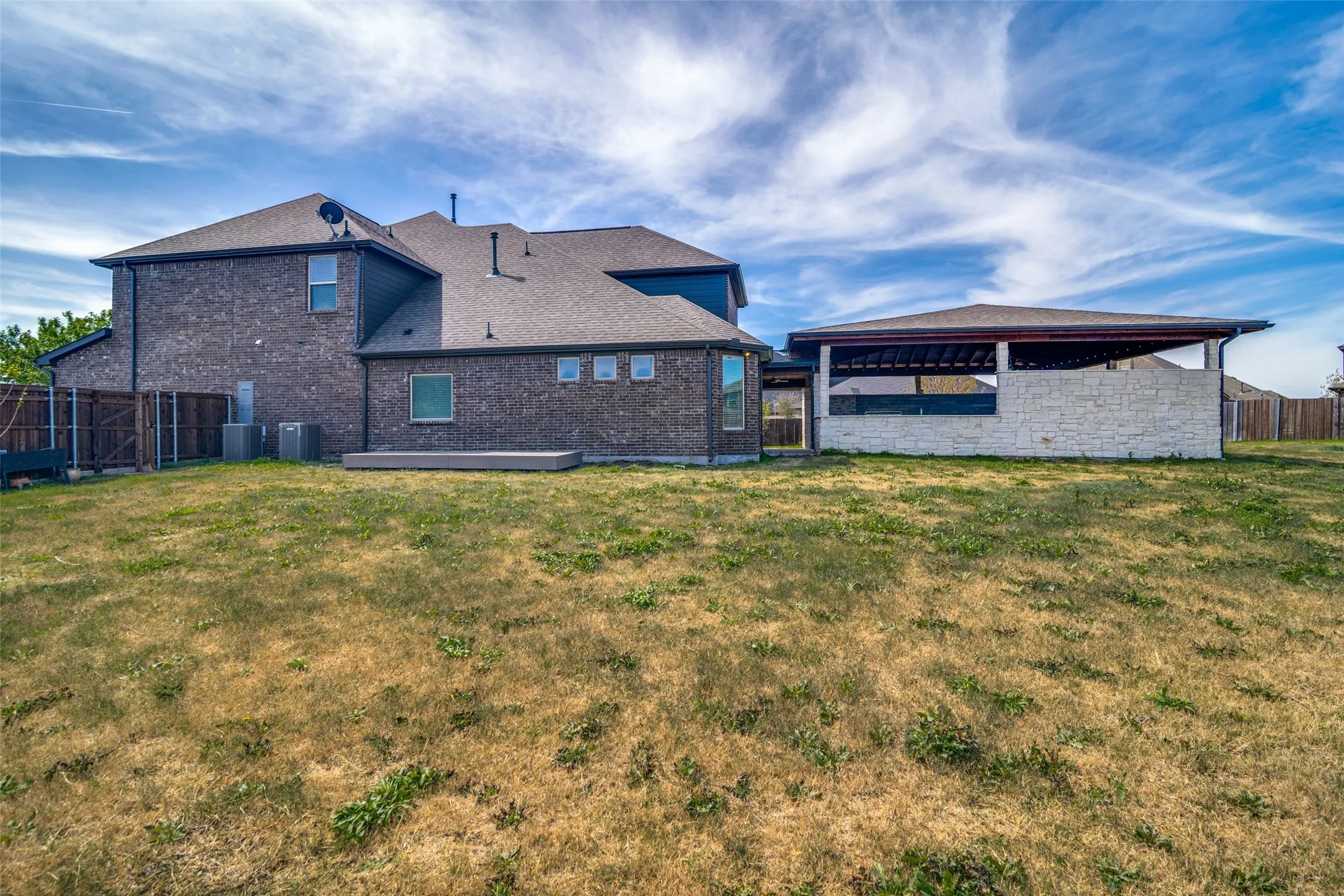 Spacious backyard featuring a covered patio with stone facade and a wood privacy fence