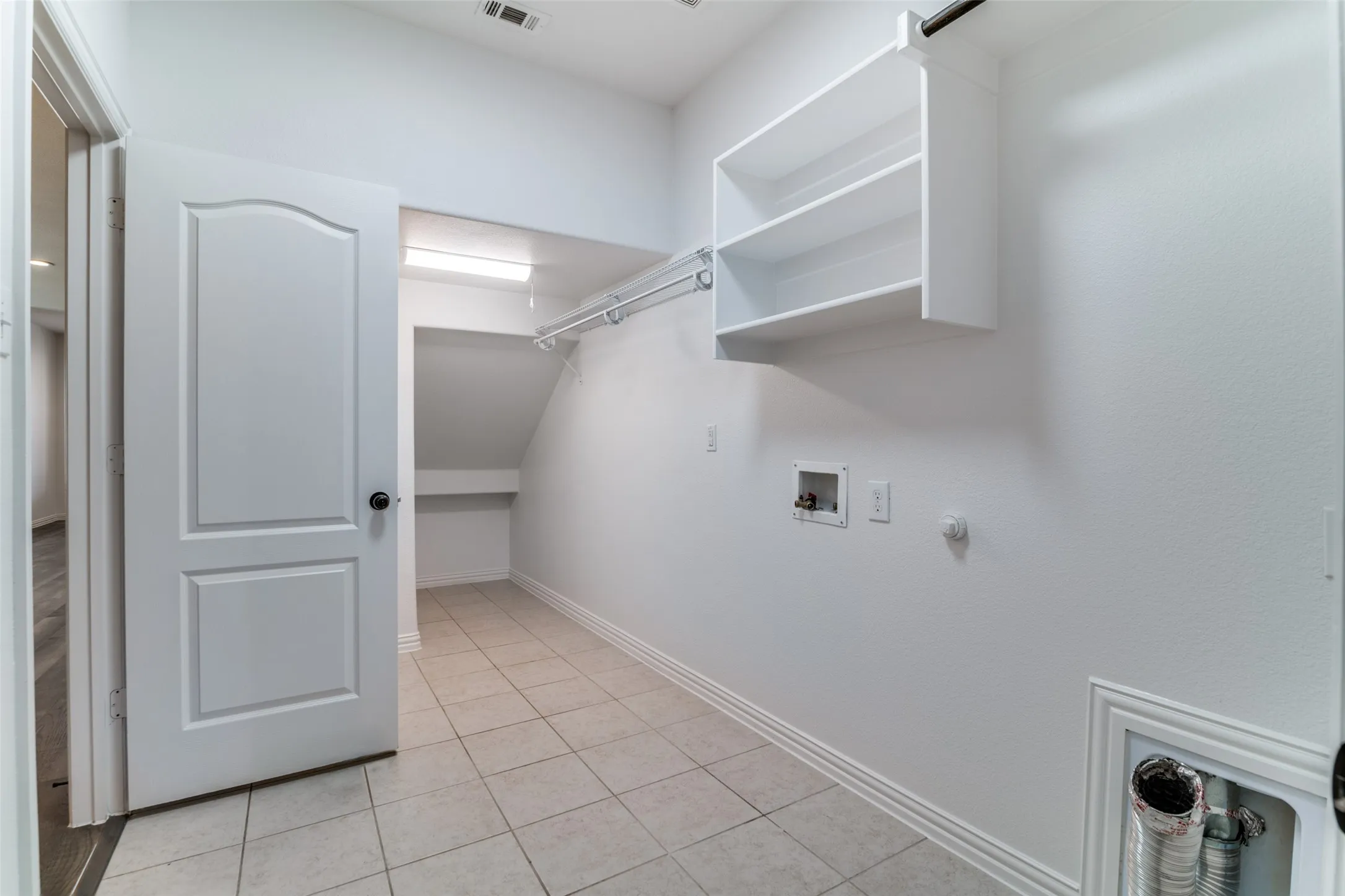 Laundry room withdryer hookup, washer hookup, and light tile patterned floors with extra space under the stairs