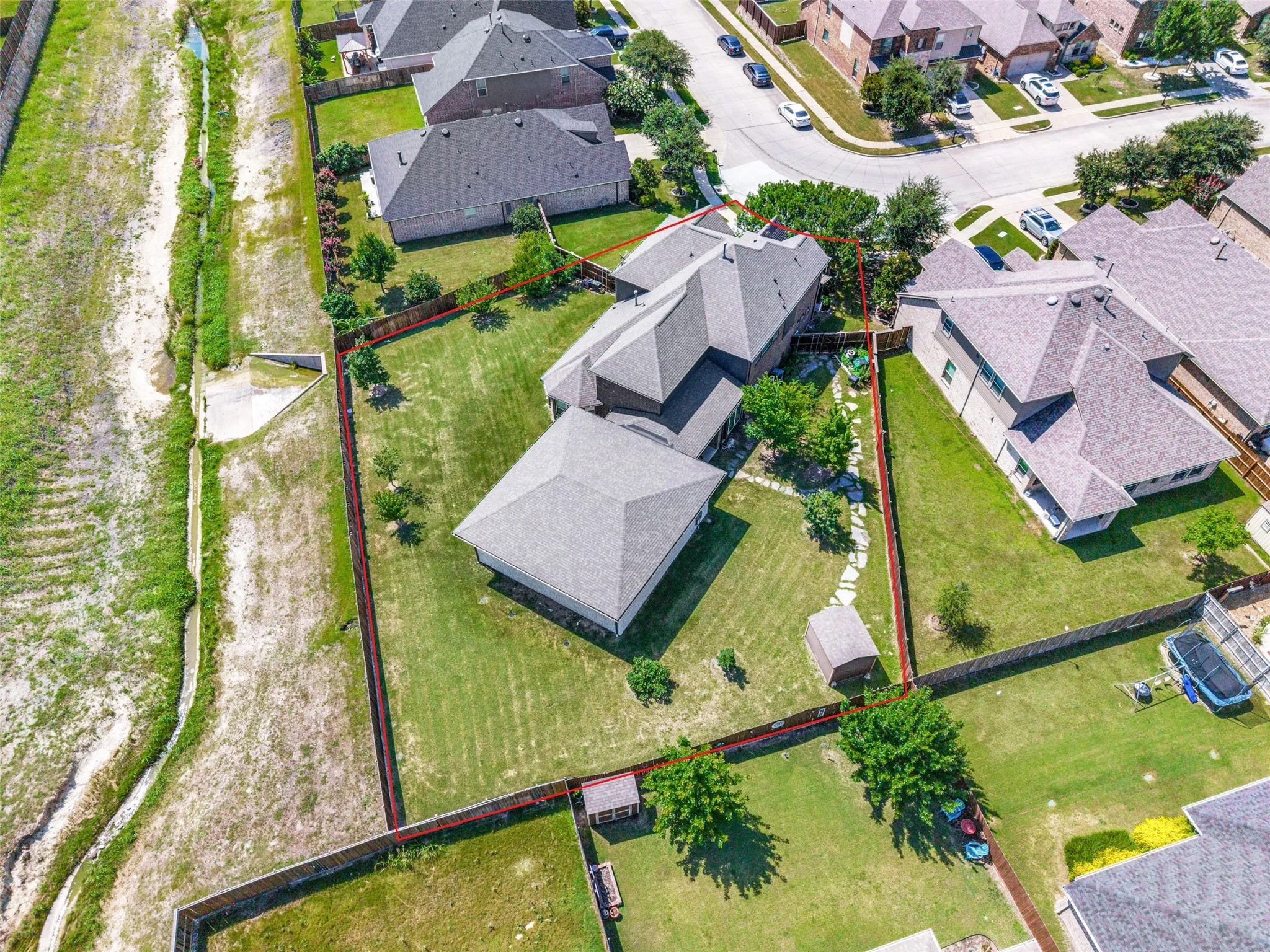 Expansive backyard featuring a manicured lawn, established trees, a storage shed, and a privacy fence