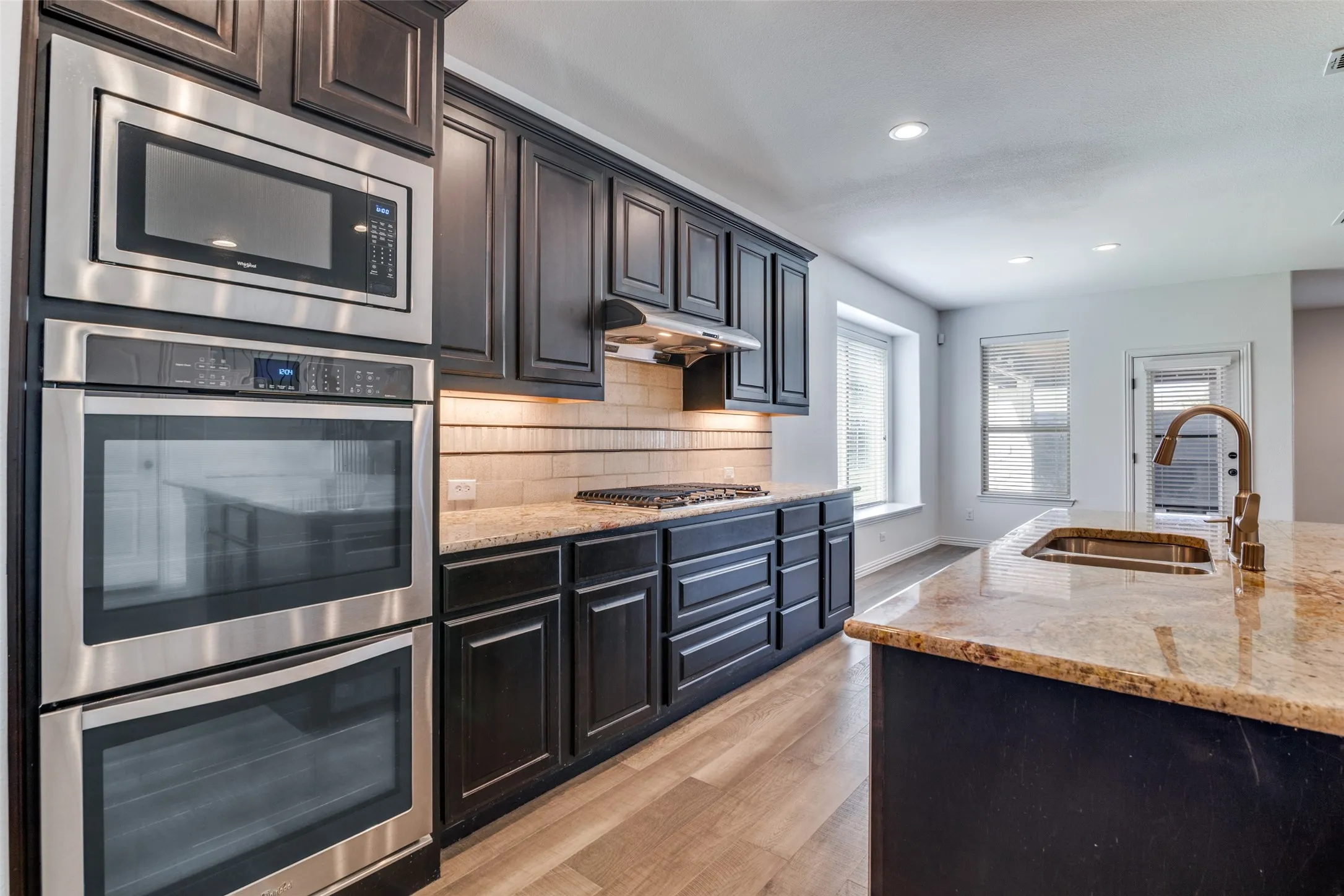 Kitchen with stainless steel appliances, light stone countertops, light wood-type flooring, decorative backsplash, and recessed lighting