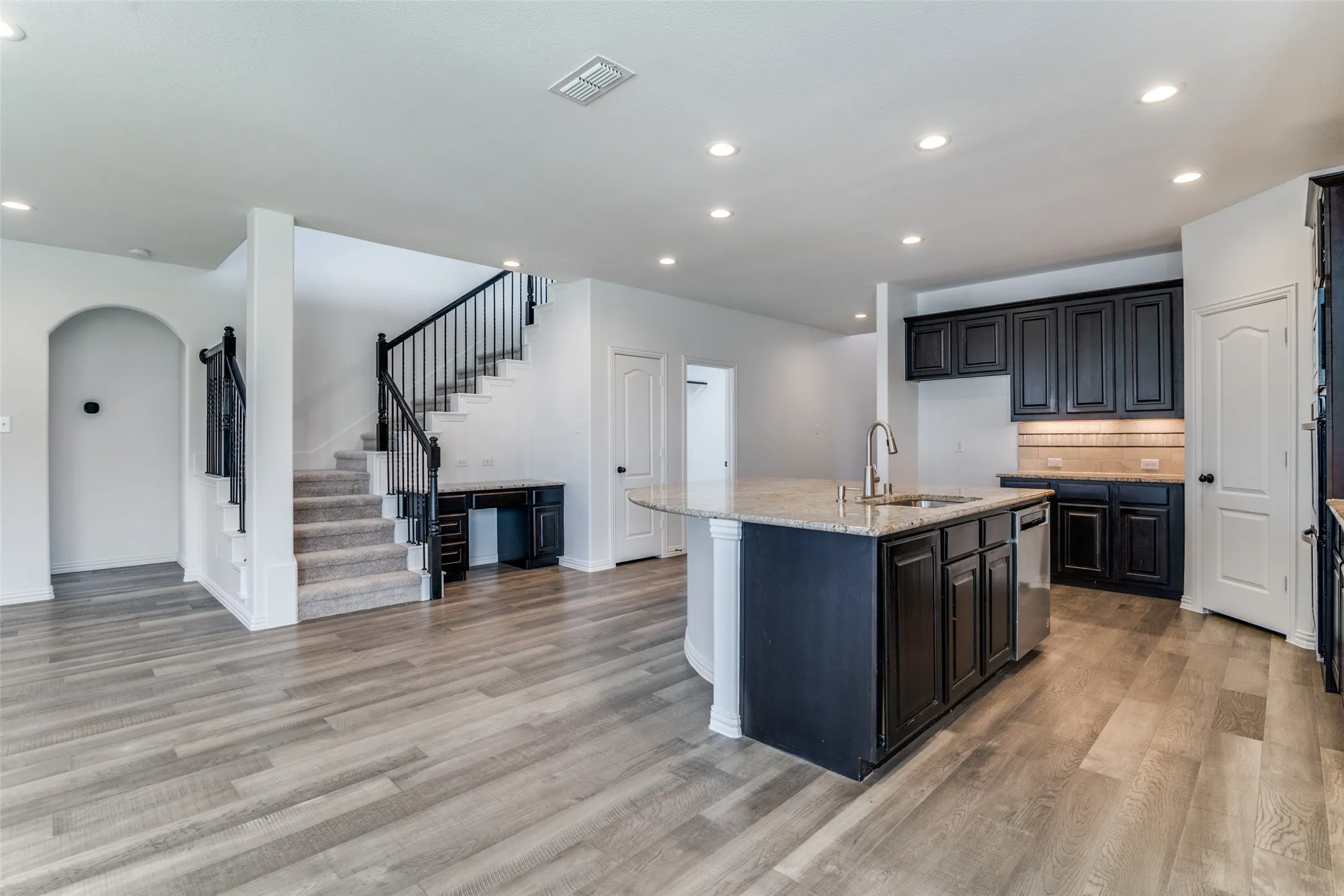 Kitchen with a center island with sink, light stone counters, recessed lighting, arched walkways, and decorative backsplash