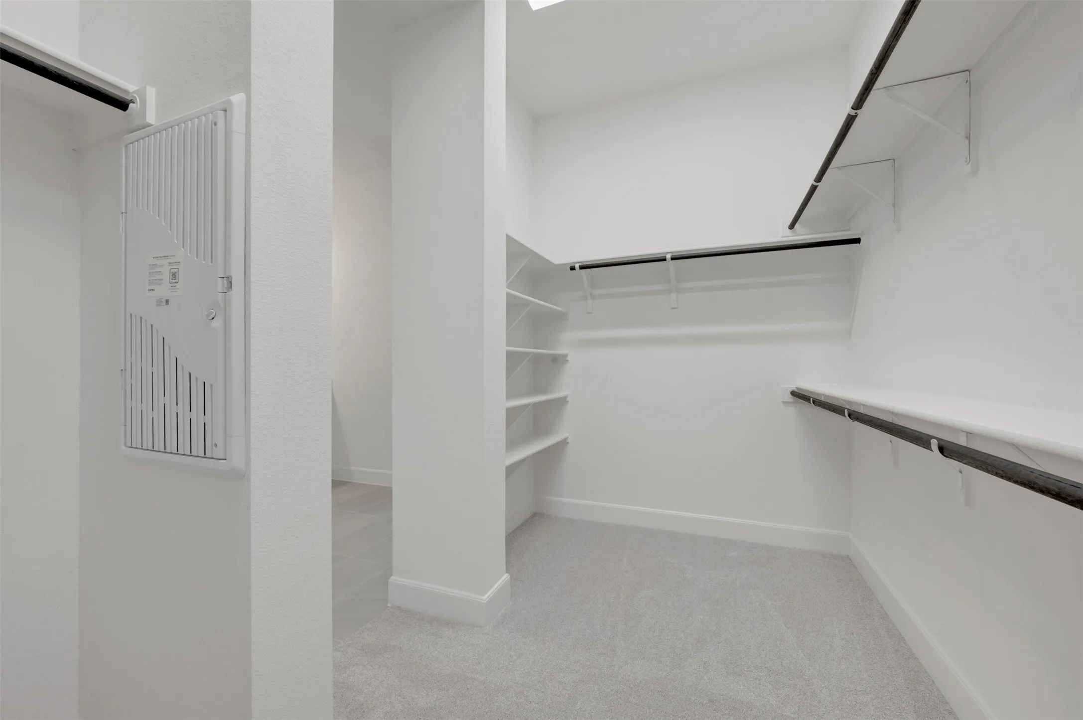 Walk-in closet featuring light gray carpet, white baseboards, multiple white shelving units, and black clothing rods