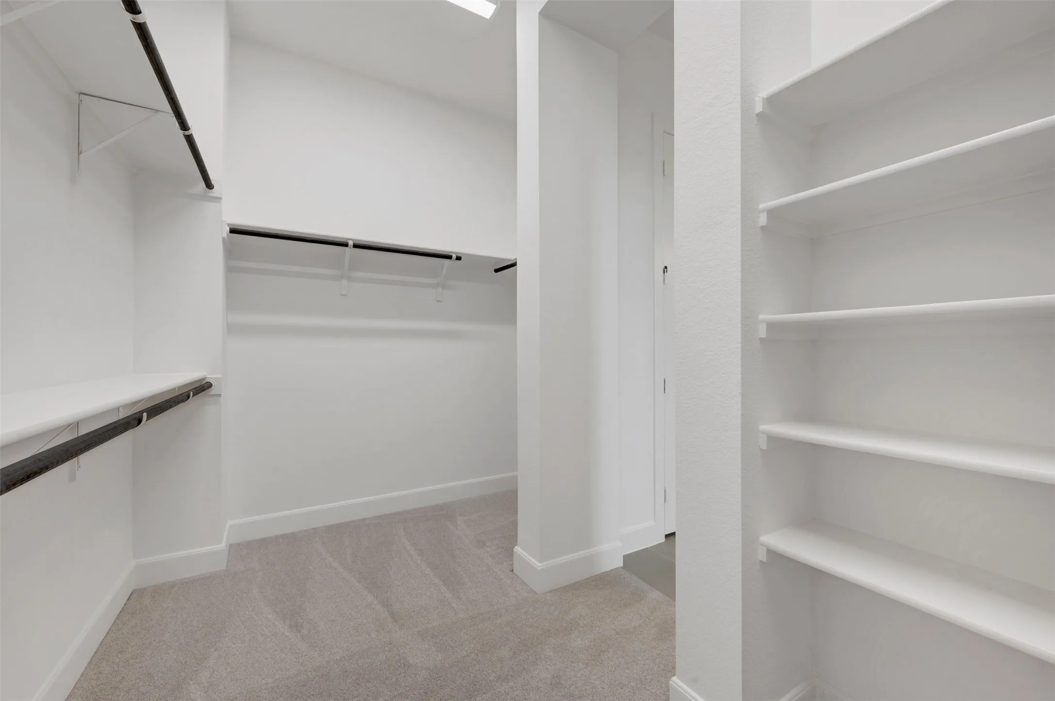 Walk-in closet featuring light gray carpeting, multiple built-in shelving units, and two levels of hanging rods for extensive storage