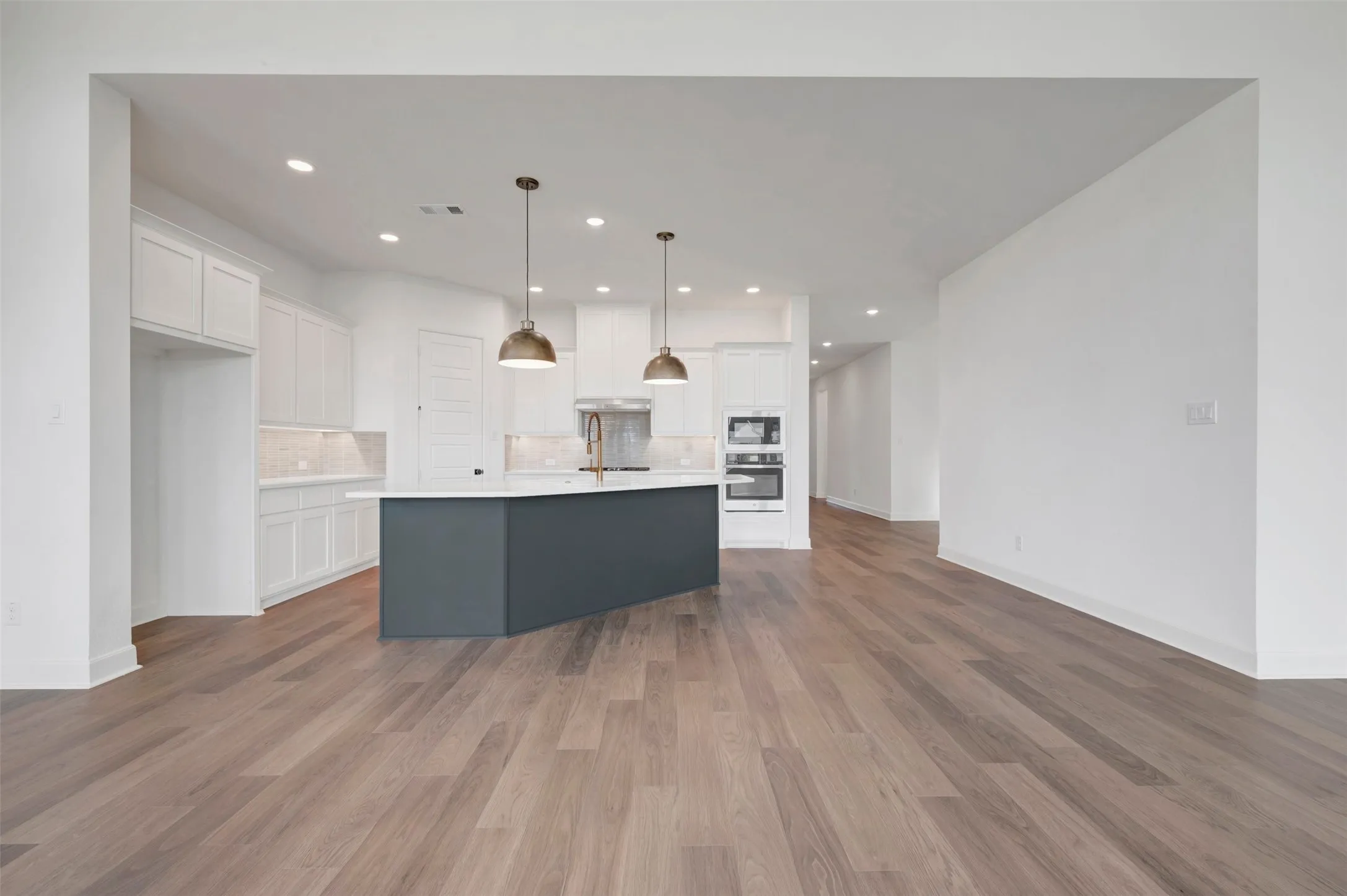 Open-concept kitchen featuring a dark blue island, recessed lighting, wood-finish flooring, white cabinetry, and built-in double ovens