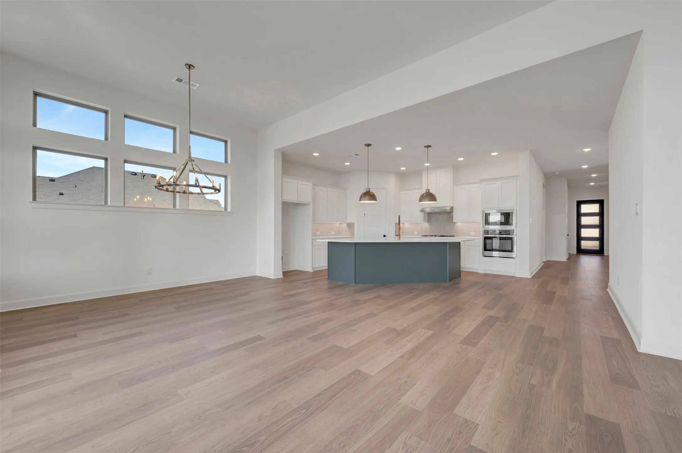 Expansive open-concept living area featuring light wood-finish flooring, a contemporary chandelier, and a multi-panel window array
