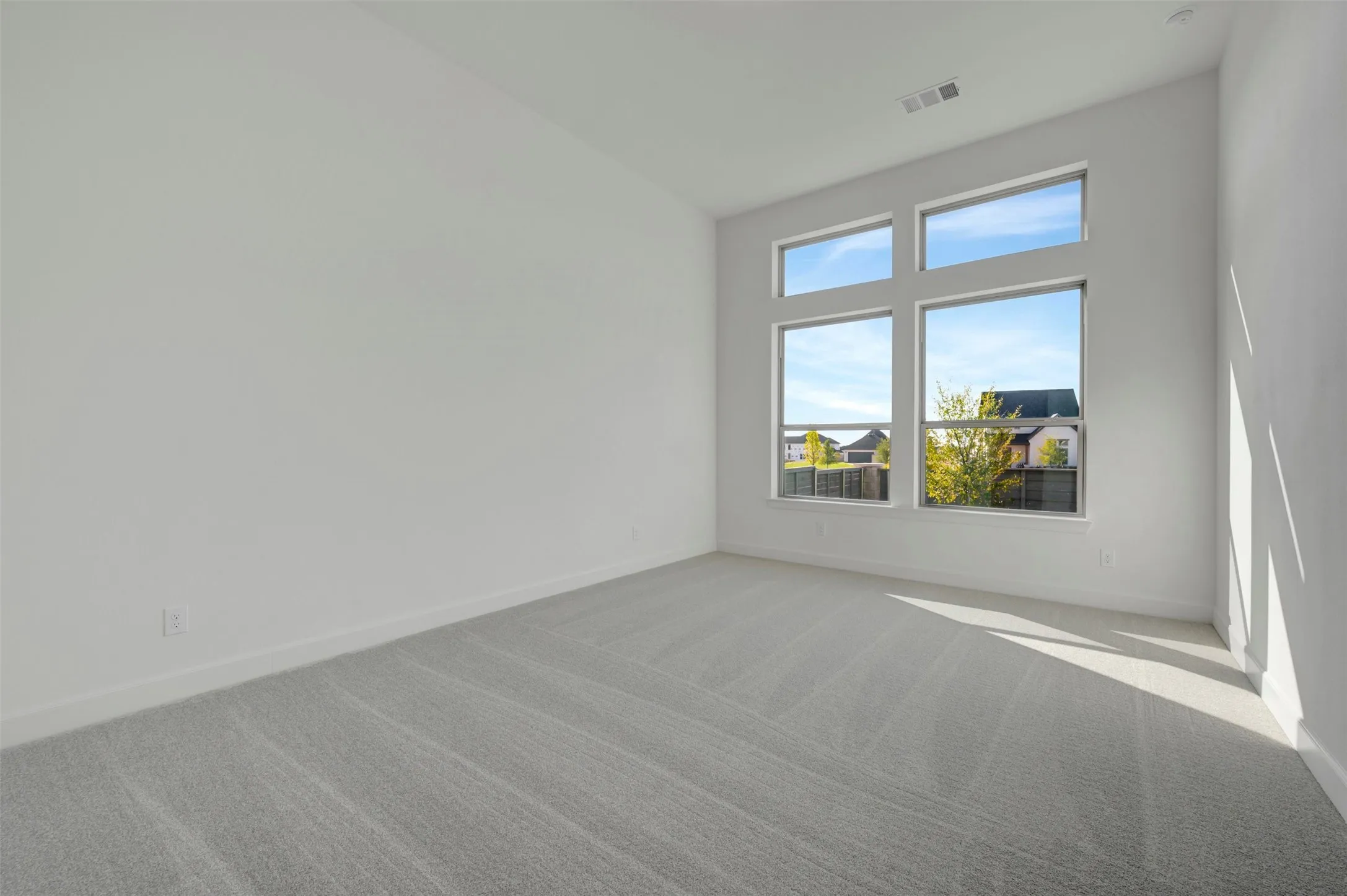 Bright interior space featuring a window wall with four large panes, light gray carpeting, crisp white walls, and white baseboards