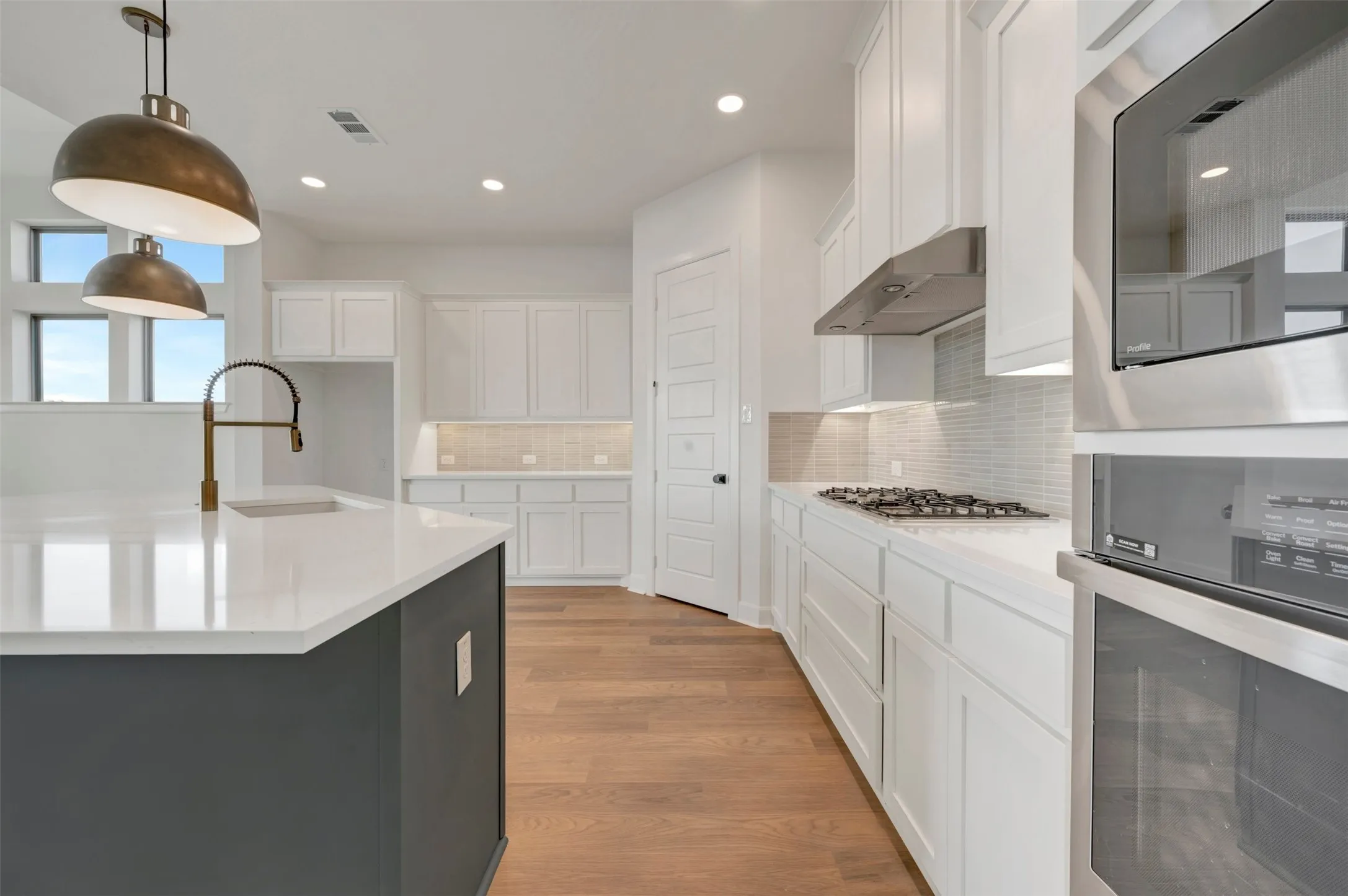 Modern kitchen featuring an island with a brass pull-down faucet and integrated sink, white shaker cabinetry, stainless steel appliances, and wood-finish flooring