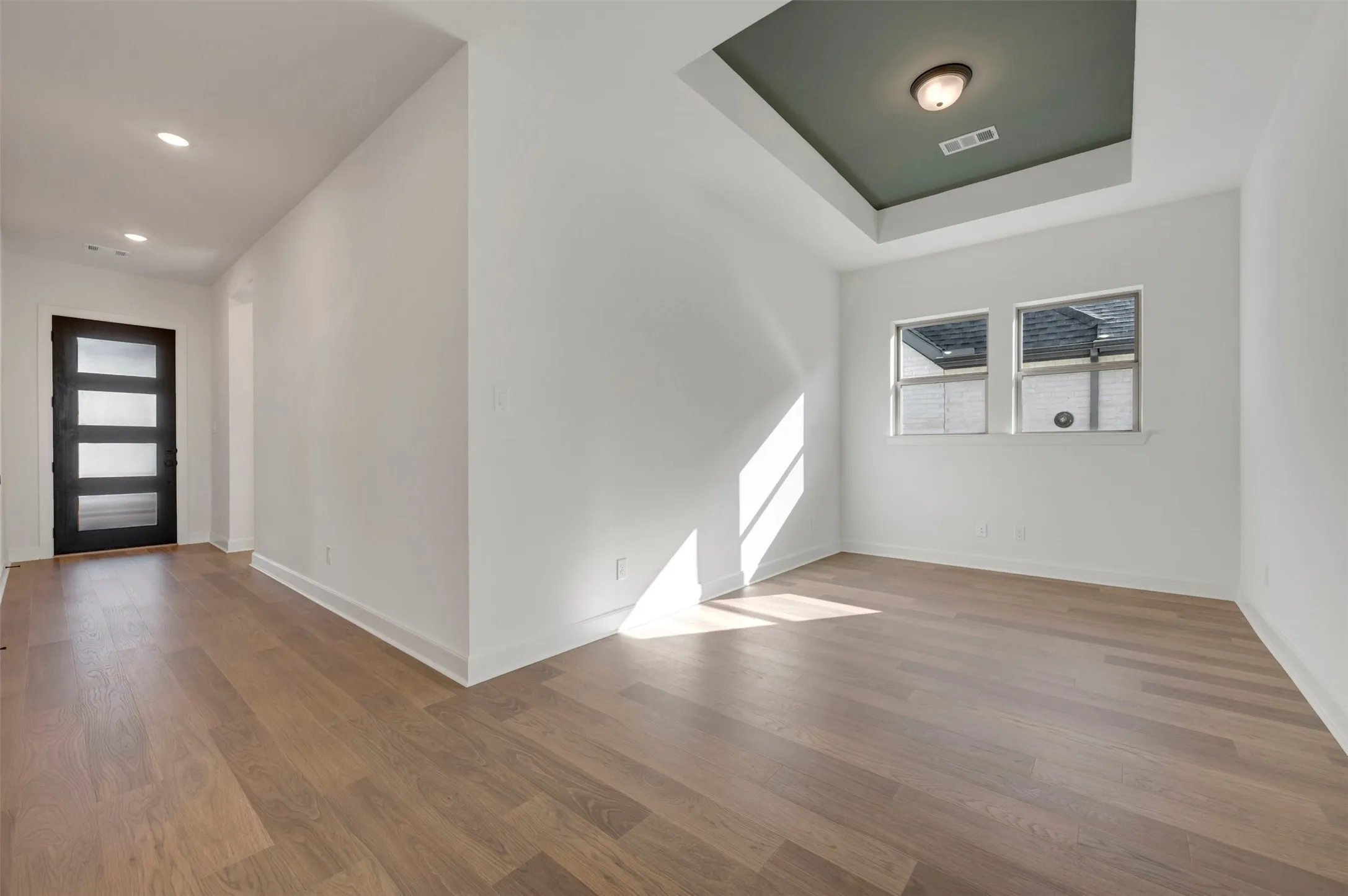 Entryway and interior room featuring wood-finish flooring, a modern black entry door with frosted glass panels, recessed lighting, and a tray ceiling with a recessed light fixture