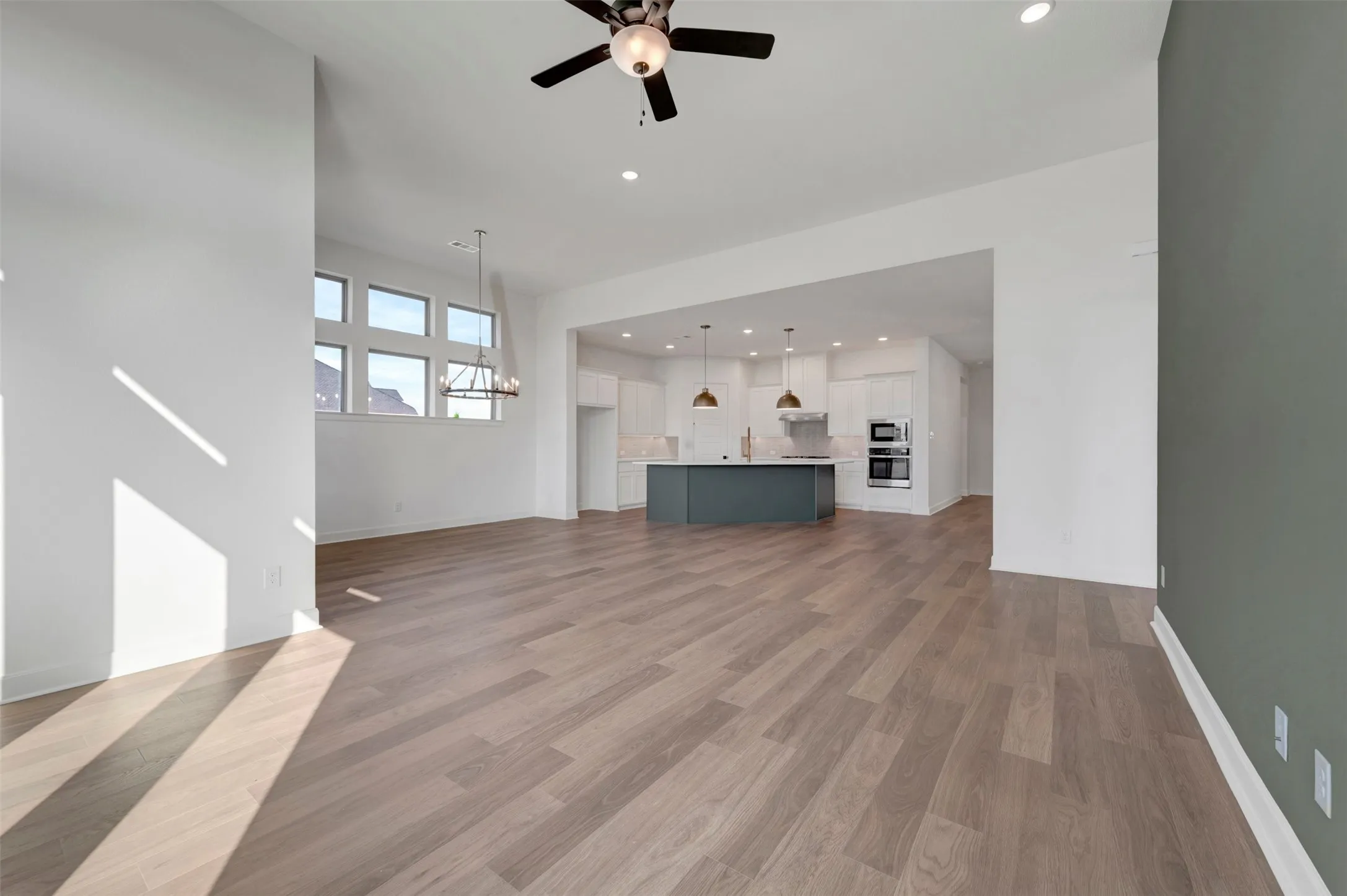 Spacious living area featuring wood-finish flooring, a contemporary chandelier, a ceiling fan, and recessed lighting