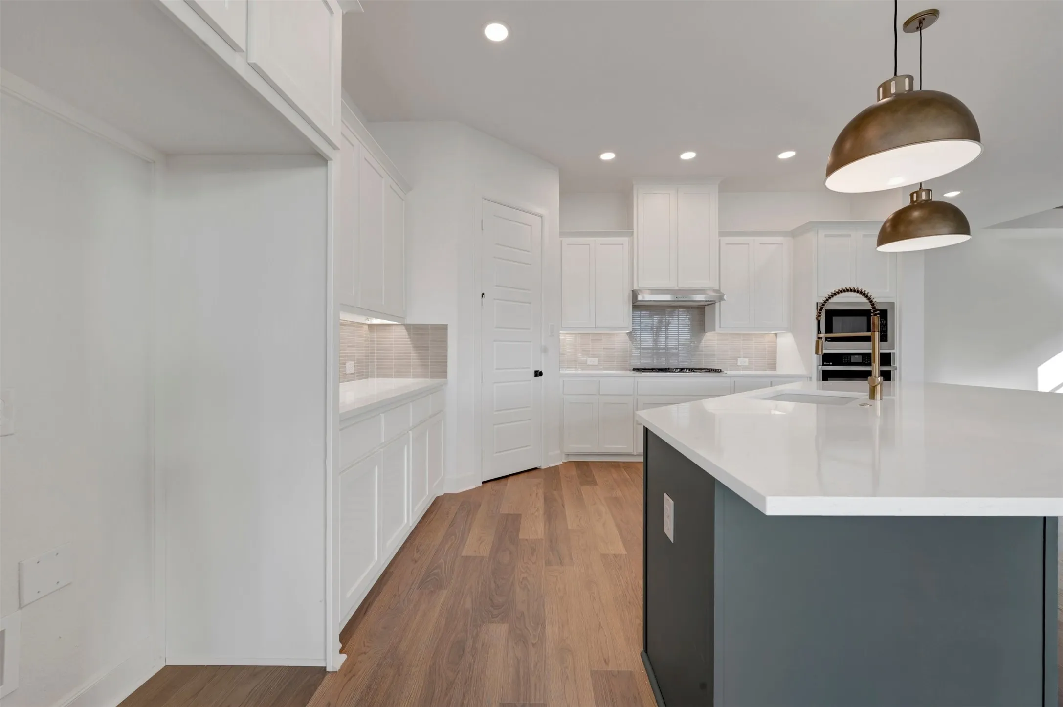 Open-concept kitchen featuring an island with a white countertop, recessed lighting, wood-finish flooring, white cabinetry, and a subway tile backsplash