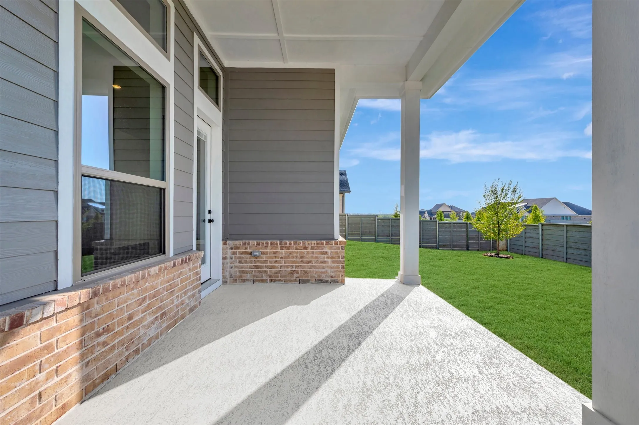 Covered patio with a concrete surface, supported by white columns, offering access to a spacious lawn