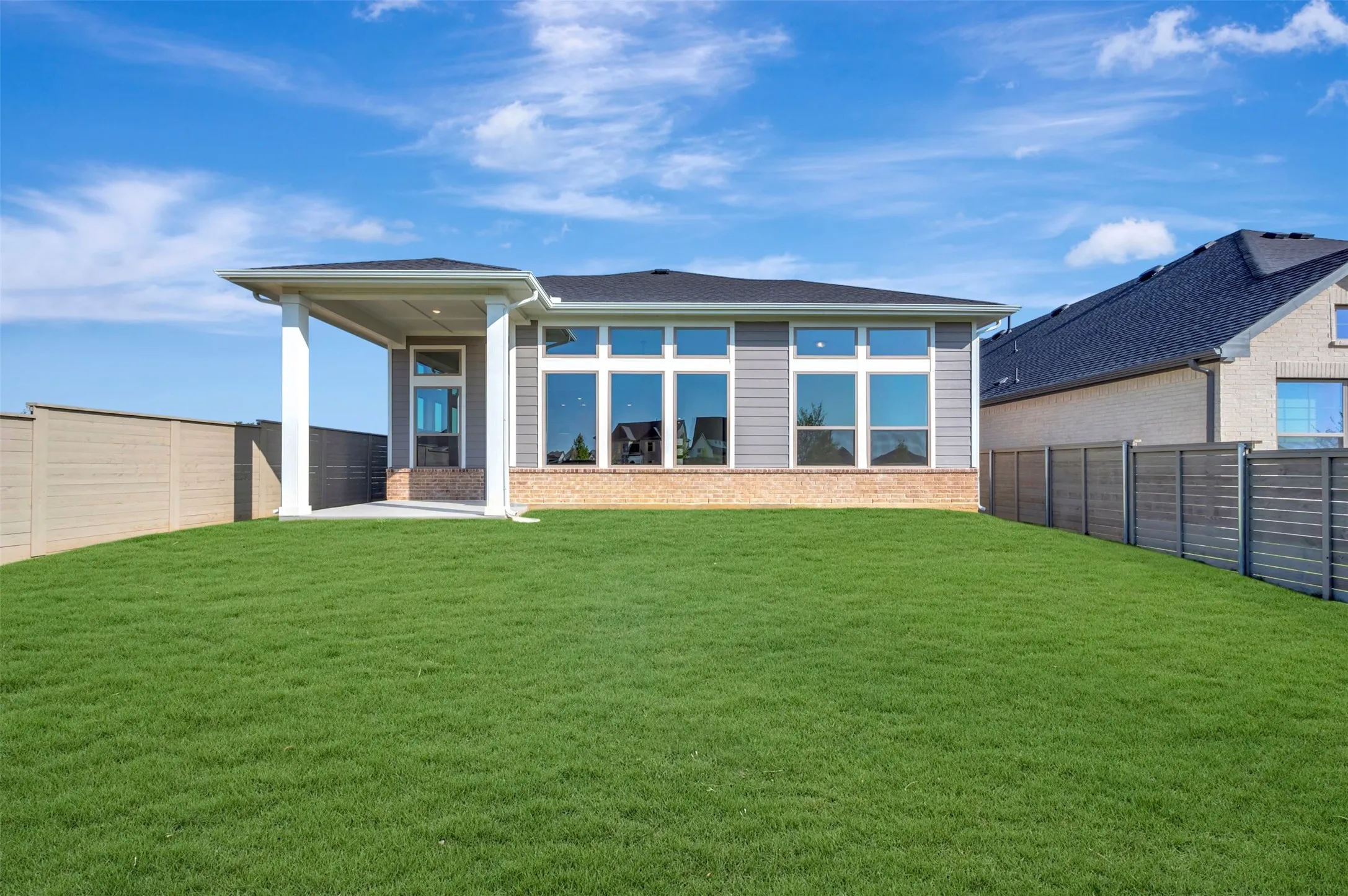 Expansive green lawn with a covered patio, featuring large windows and horizontal siding