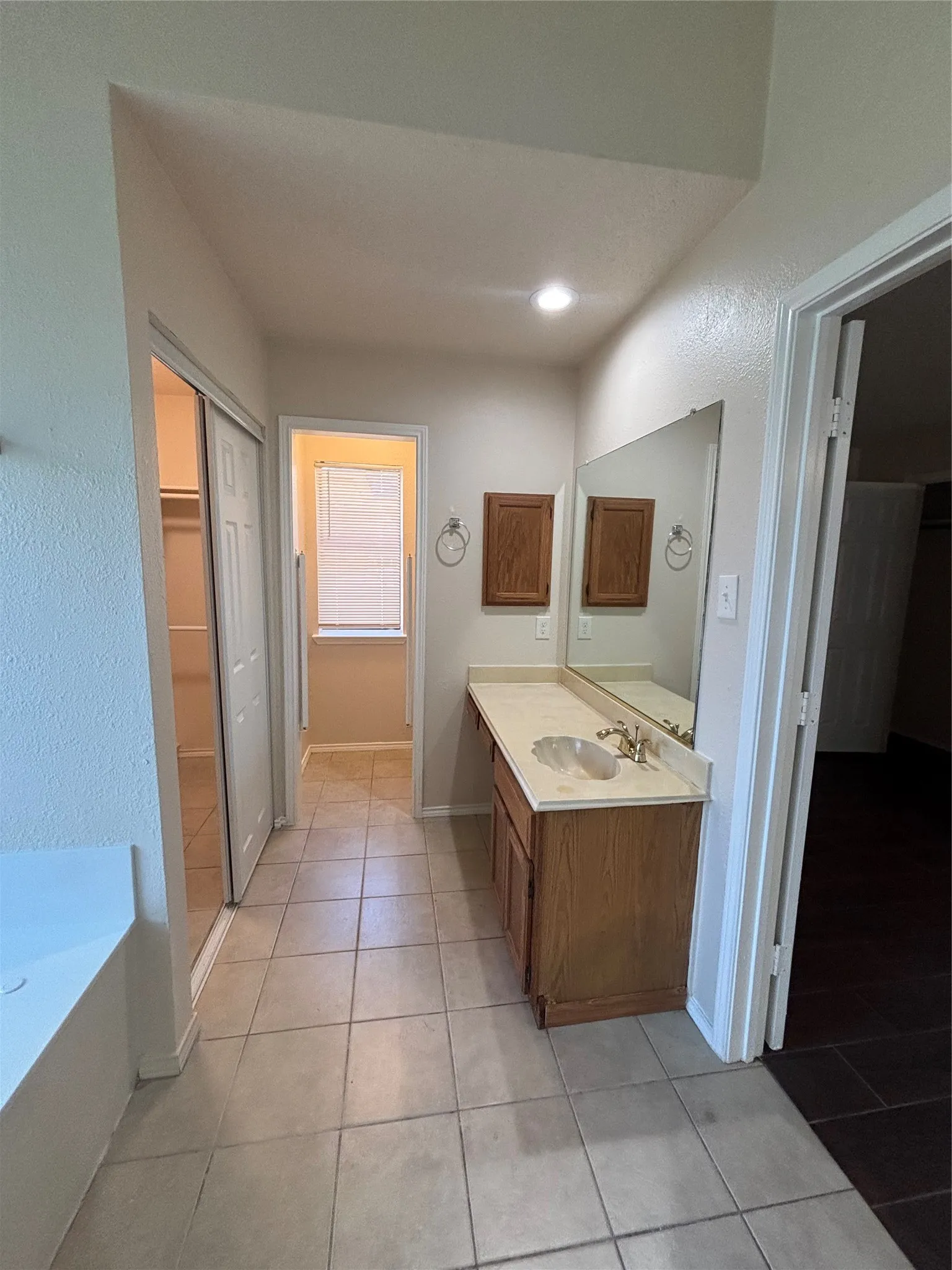 Bathroom with vanity, a bath, light tile patterned floors, a spacious closet, and a textured wall