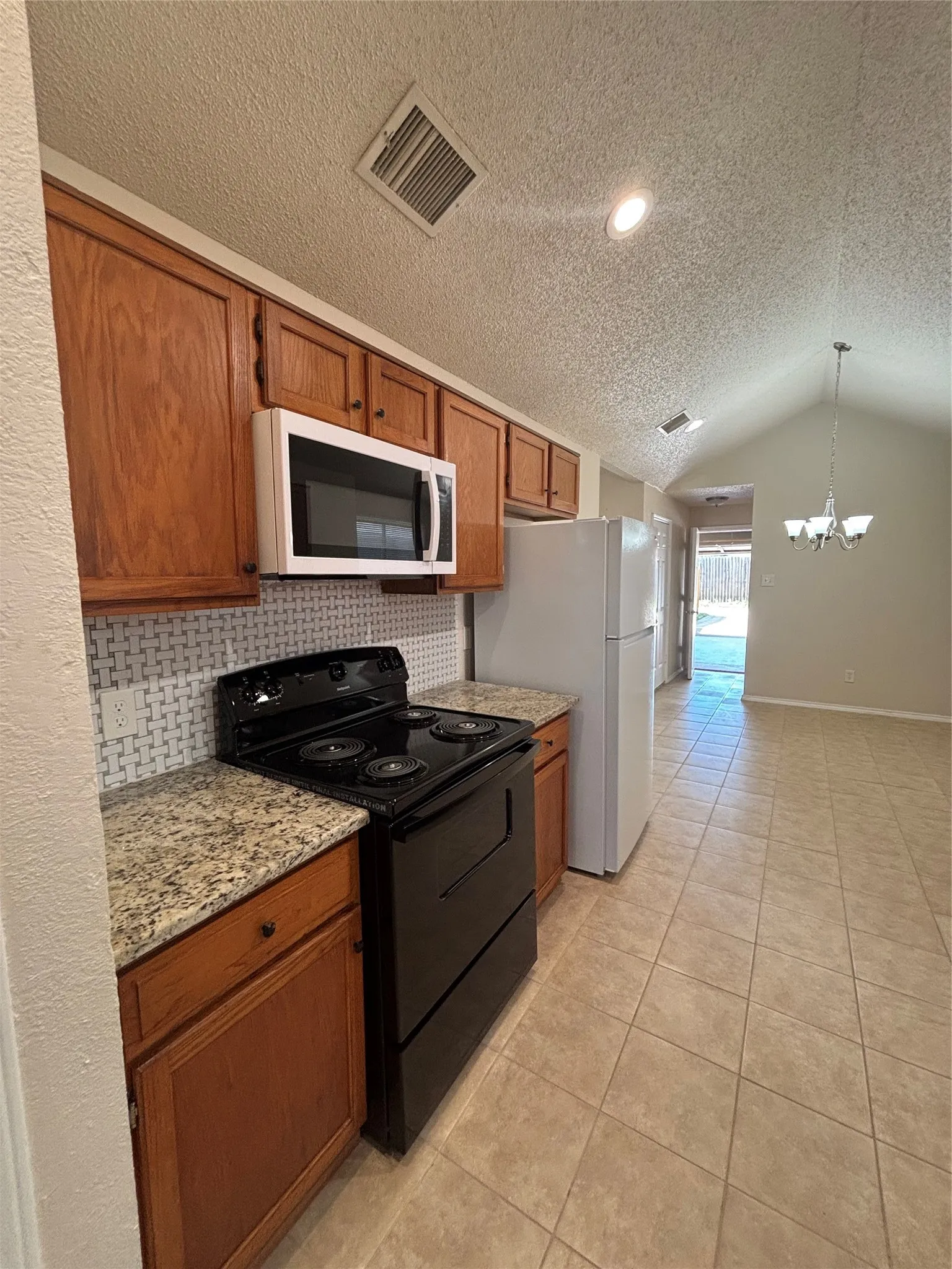 Kitchen with white appliances, a textured ceiling, wood finish cabinets, suspended lighting, and light tile patterned floors