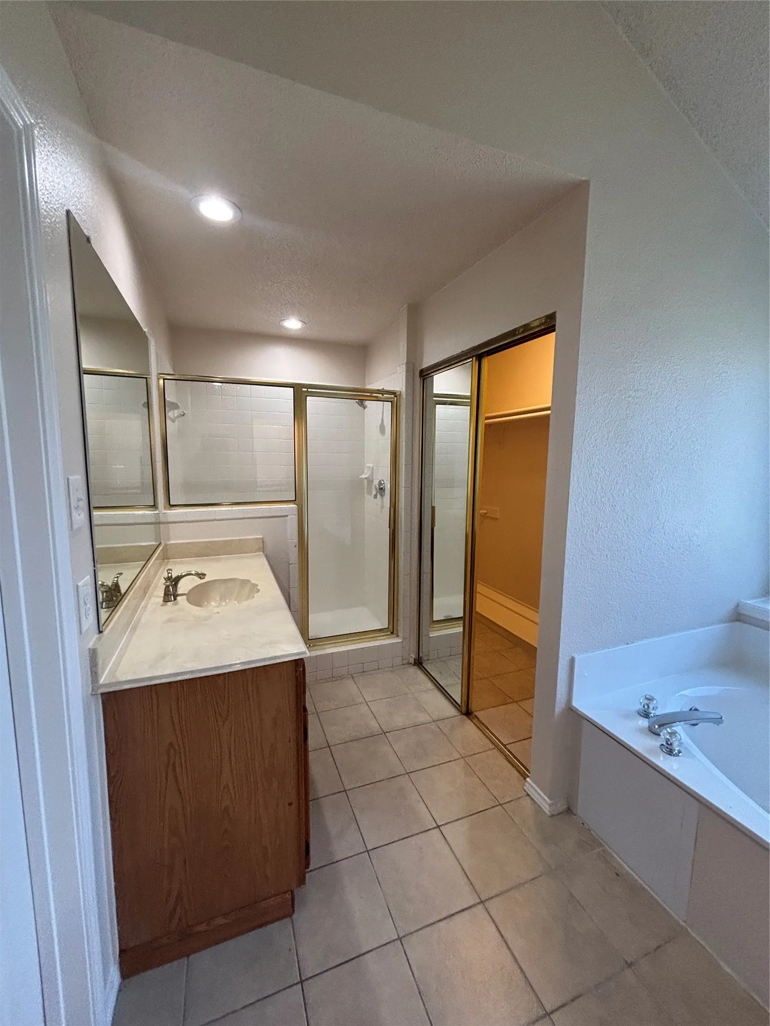 Bathroom with a garden tub, a stall shower, vanity, light tile patterned flooring, and a textured wall