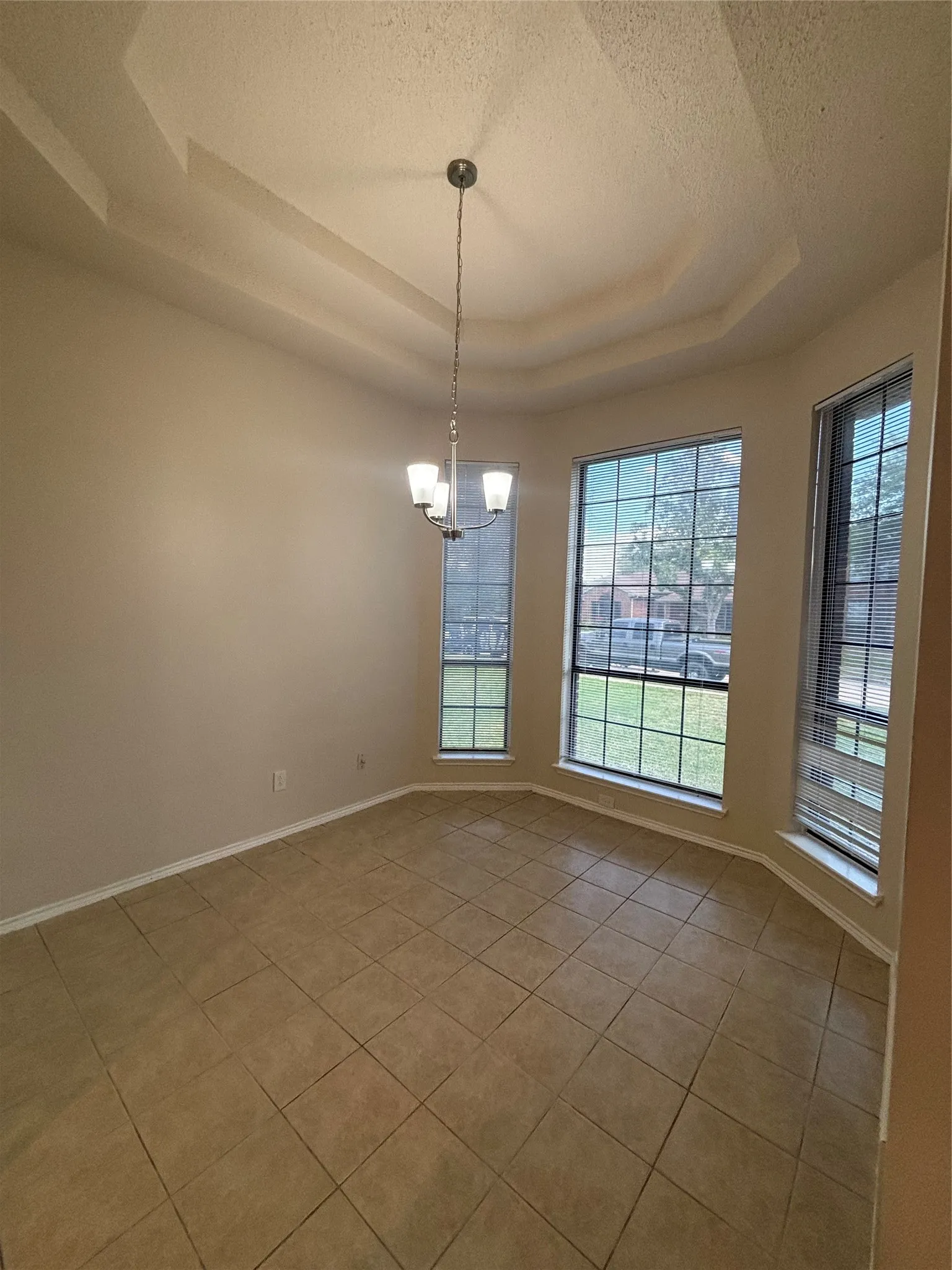 Spare room with a textured ceiling, light tile patterned floors, a raised ceiling, and a chandelier