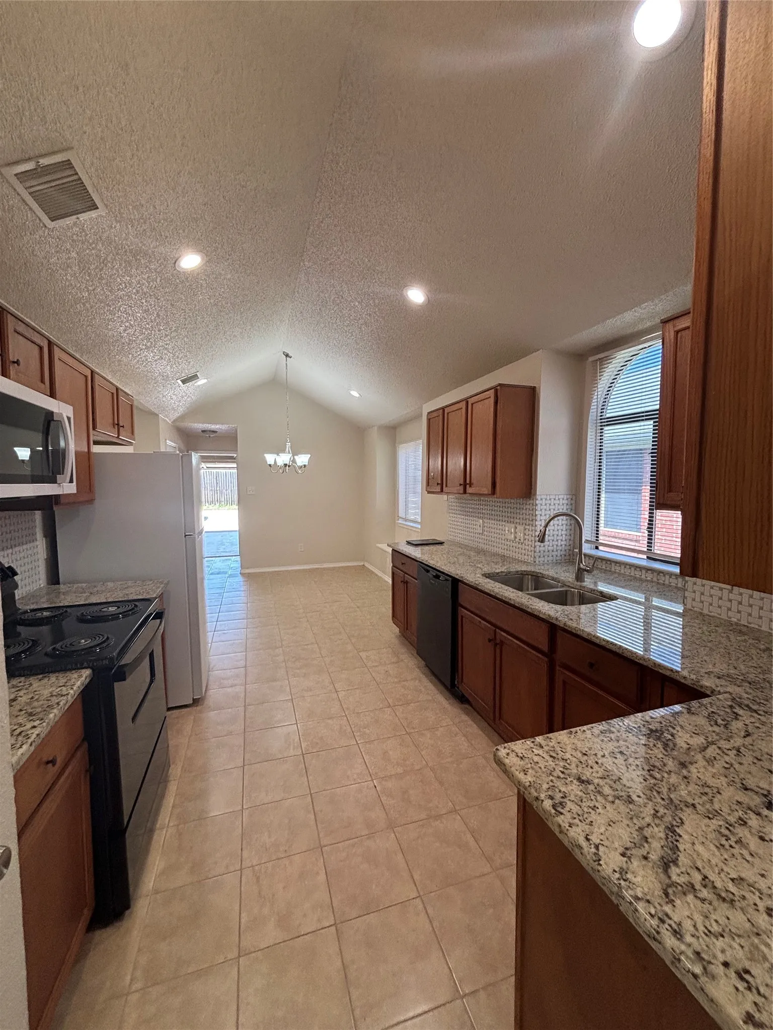 Kitchen featuring tasteful backsplash, black appliances, light stone counters, suspended lighting, and wood finish cabinets