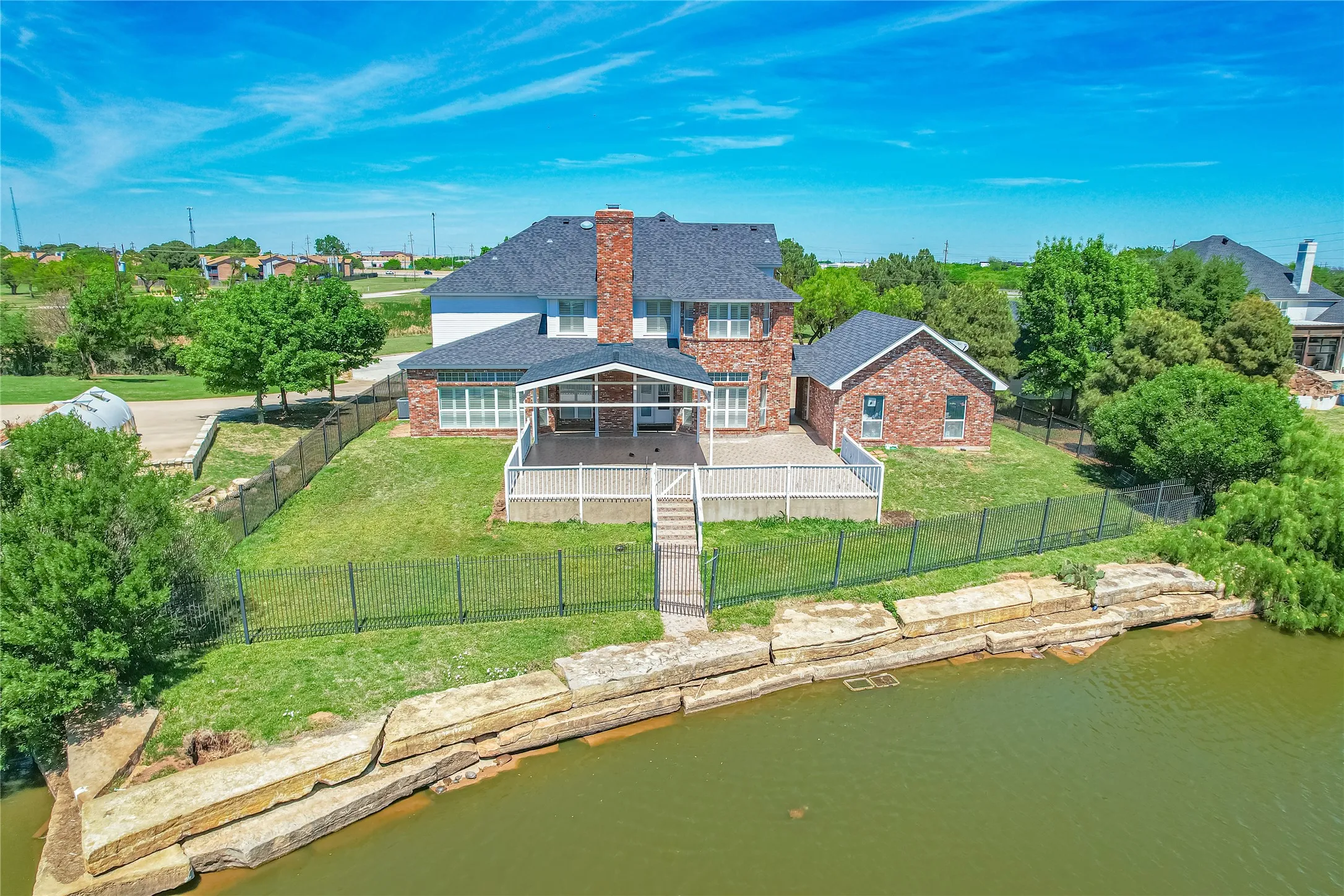 Back of house featuring a water view, brick siding, a chimney, a fenced backyard, and roof with shingles