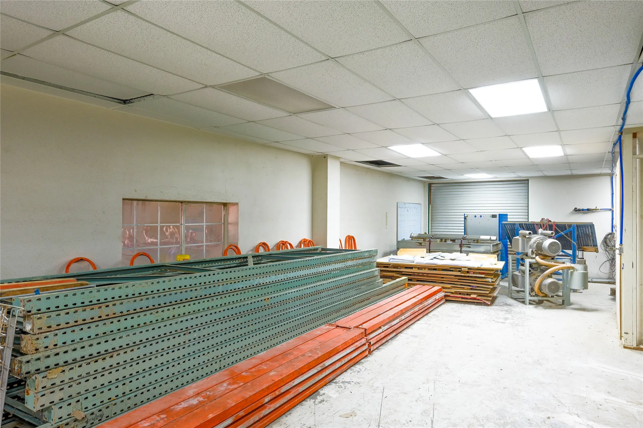 Spacious interior room featuring concrete flooring and a drop ceiling with recessed square lighting