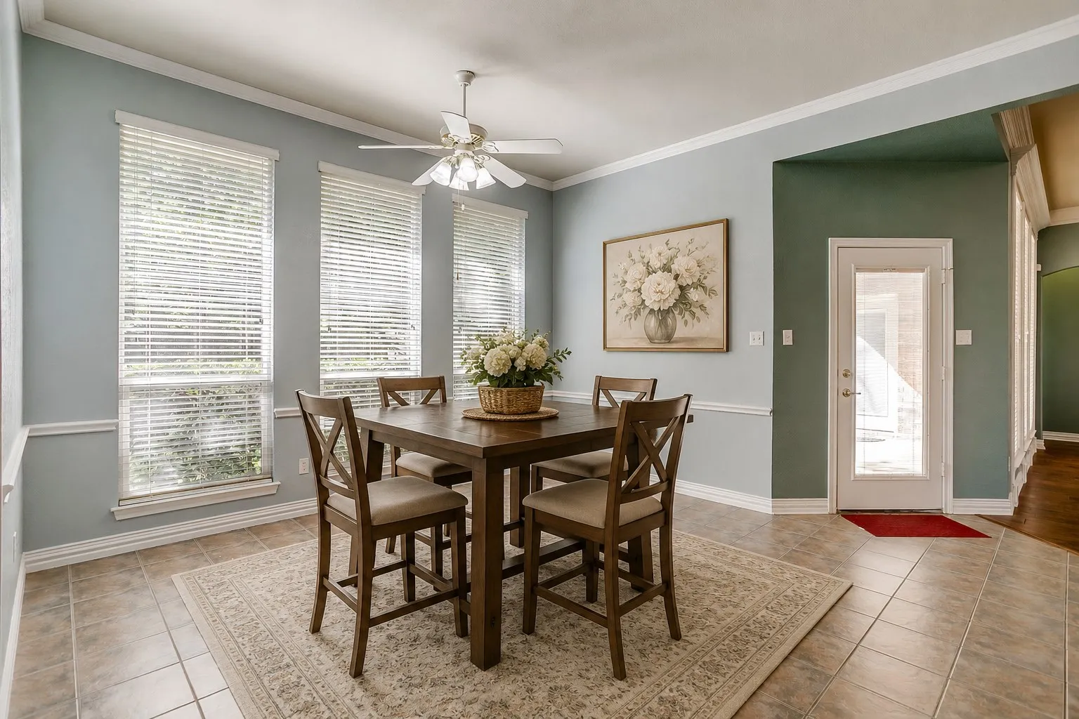 Dining space featuring tile flooring, three large windows with blinds, a ceiling fan with integrated lighting, and crown molding