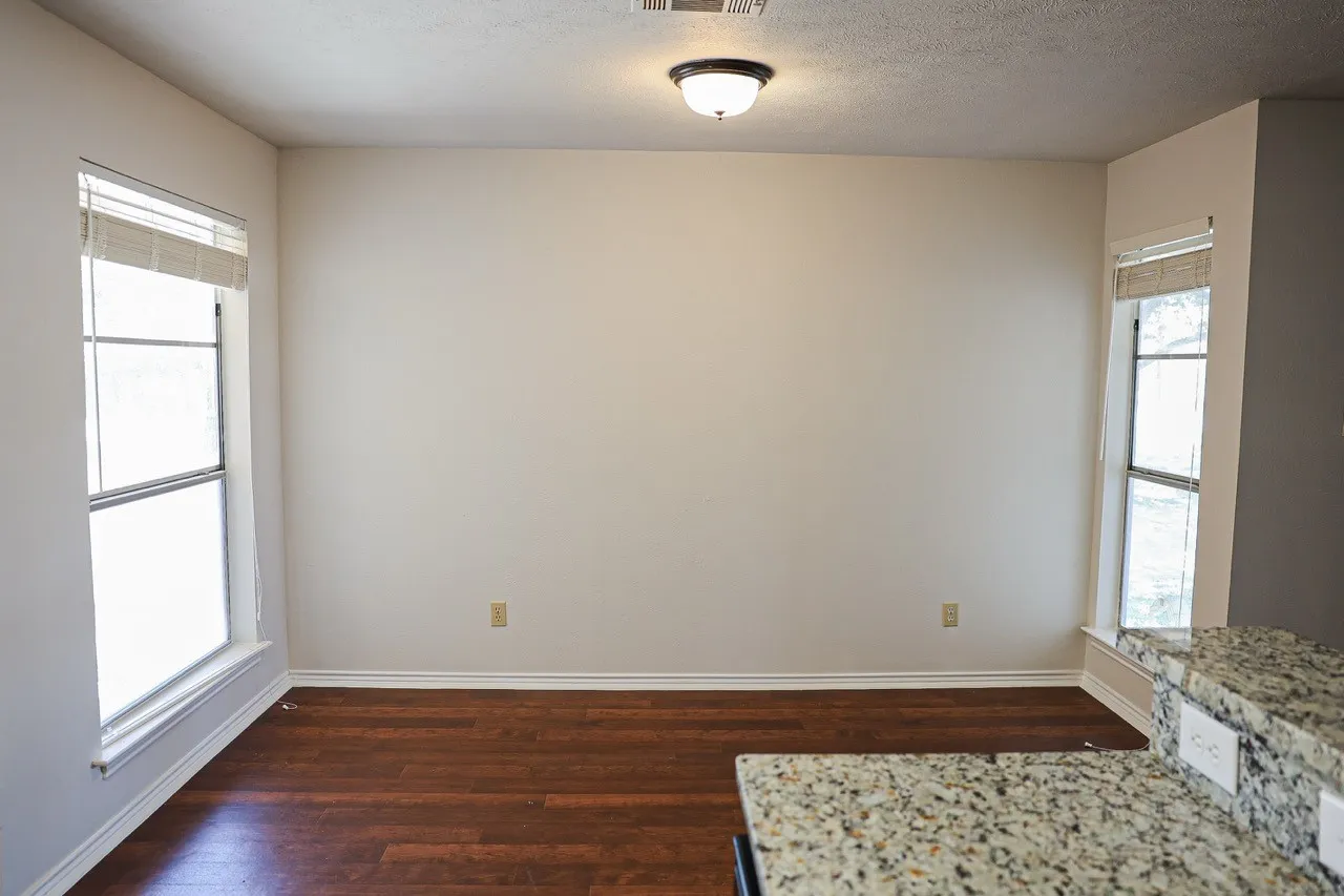 Bright interior space featuring wood-finish flooring and two windows with blinds