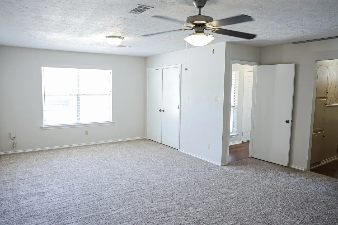 Spacious room featuring neutral carpeting, a large window with horizontal blinds, and a ceiling fan with integrated lighting