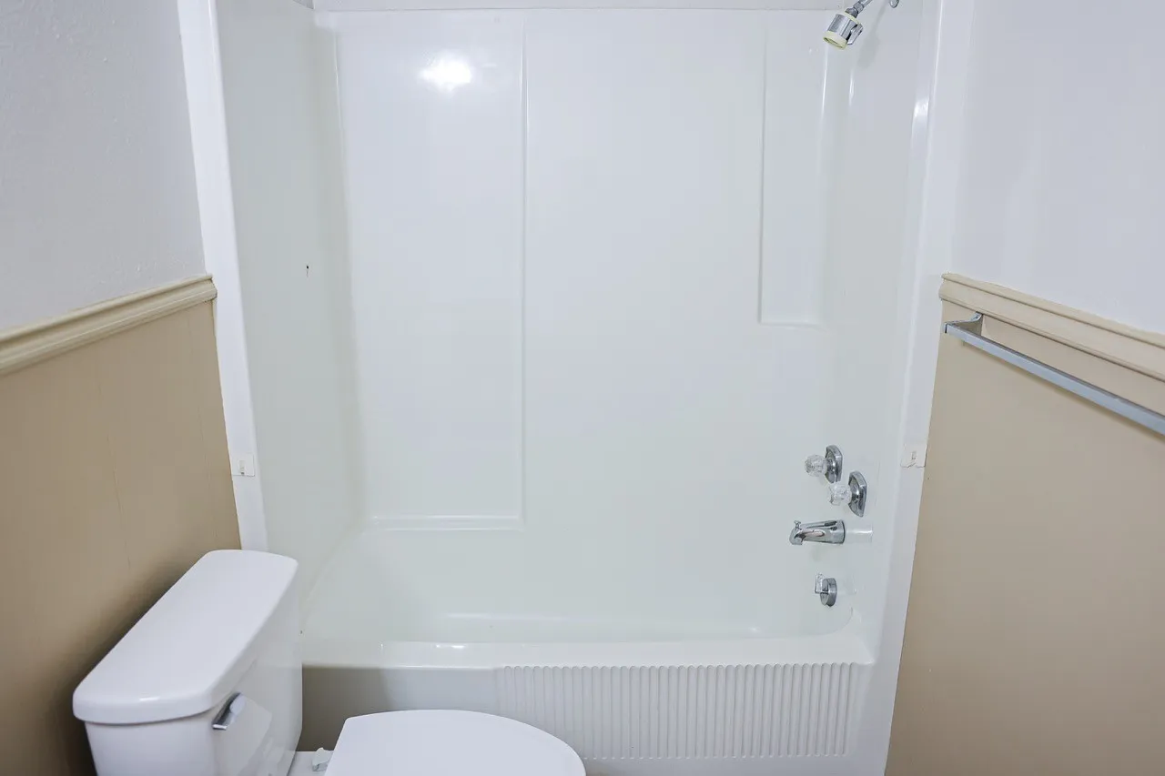 White tub and shower combination with chrome fixtures, a fluted tub panel, and a coordinated toilet