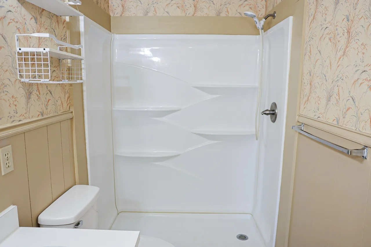 White shower enclosure featuring integrated shelving, a chrome shower head, and a single lever handle
