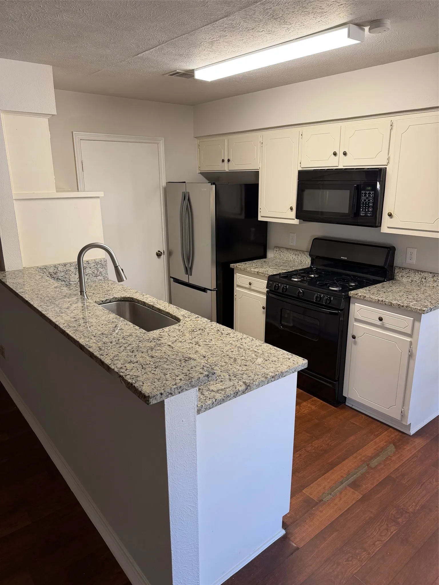 Kitchen featuring wood-finish flooring, white cabinetry, speckled countertops, a double-basin sink with a curved faucet, and a black range with an overhead microwave
