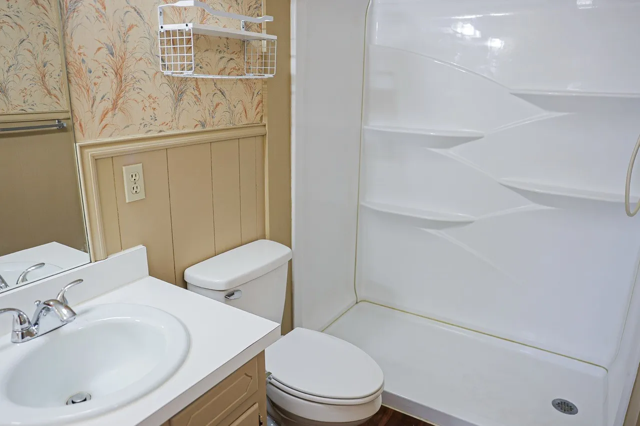 Bathroom with a white vanity and integrated sink, chrome faucet, white toilet, and a stand-up shower with built-in shelving
