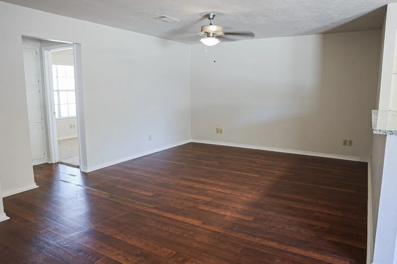 Spacious room featuring wood-finish flooring, light neutral wall paint, and a ceiling fan with integrated lighting