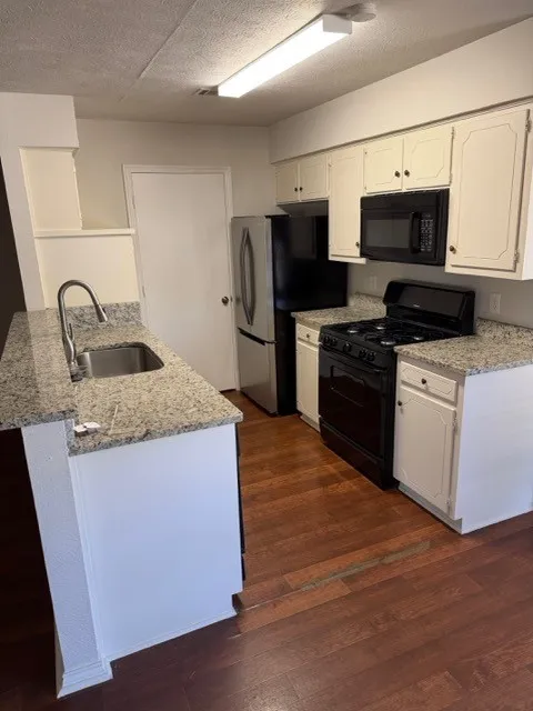 Kitchen featuring wood-finish flooring, light-toned cabinetry, stainless steel appliances, and granite-style countertops