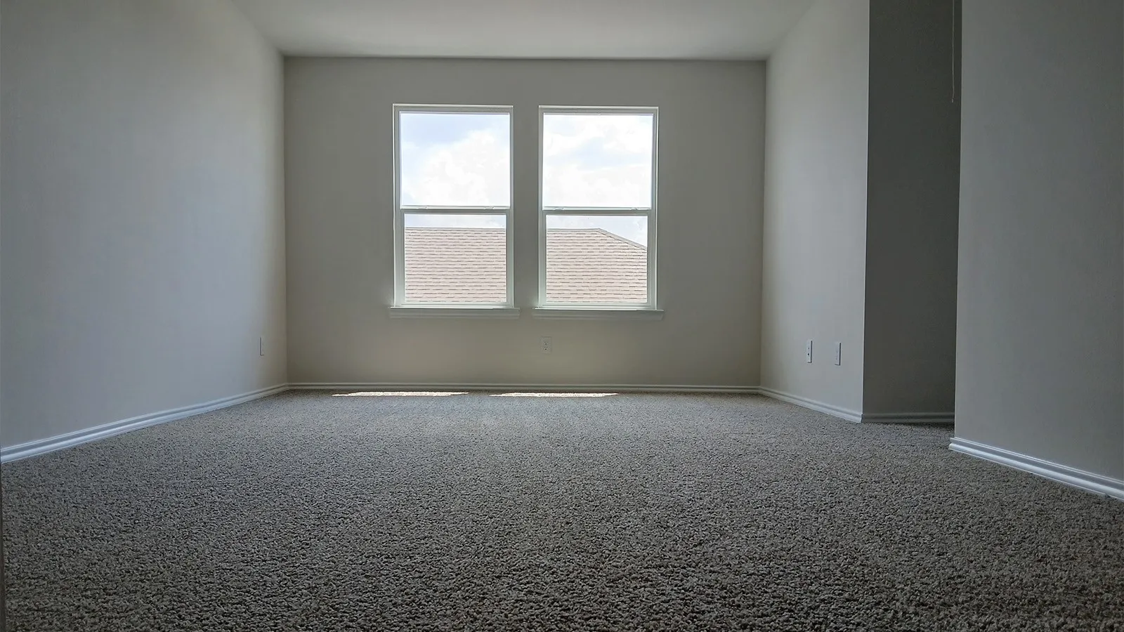 Spacious room featuring neutral carpeting, light-toned walls, and white baseboards