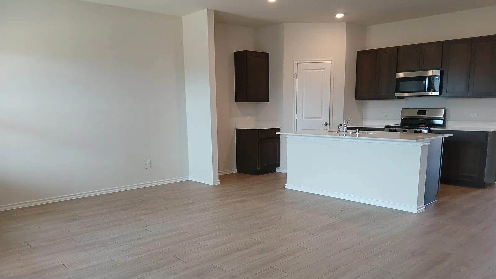 Contemporary kitchen featuring dark wood cabinetry, stainless steel appliances, a center island with a double basin sink, and wood-finish flooring