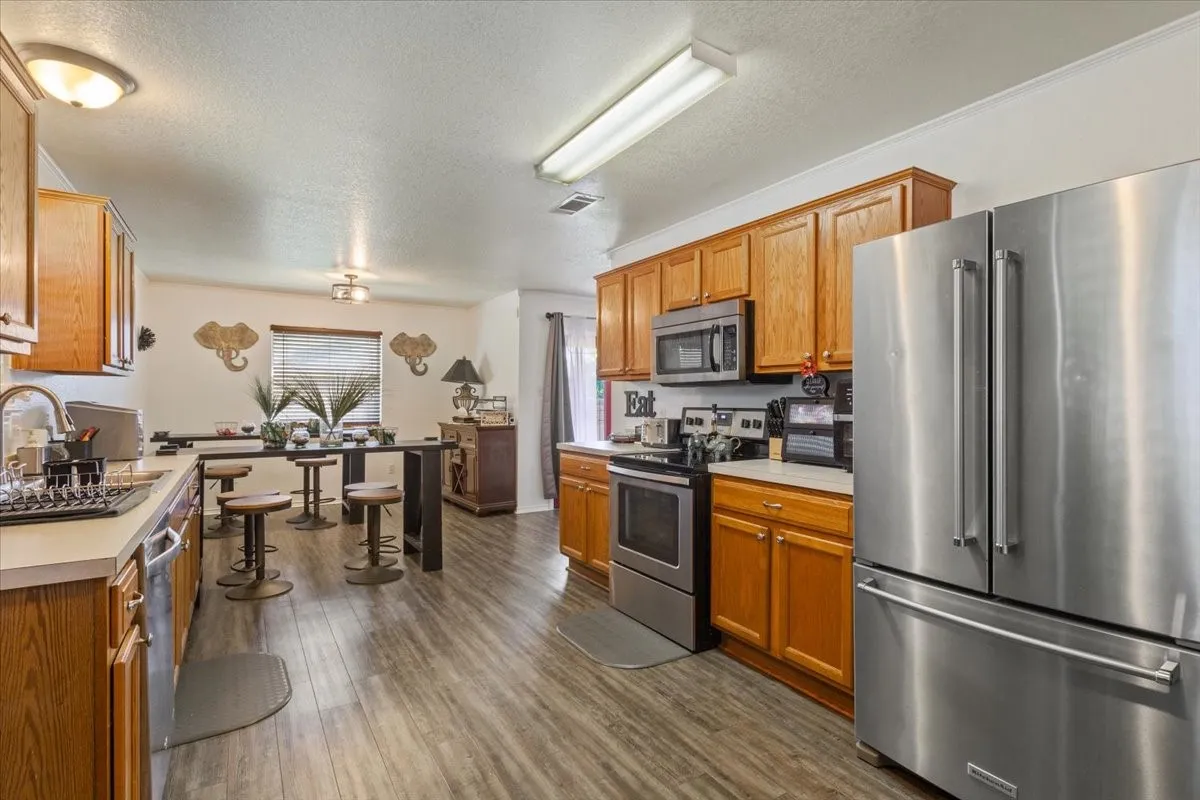 Kitchen with stainless steel appliances, light countertops, a textured ceiling, dark wood-style flooring, and wood finish cabinetry