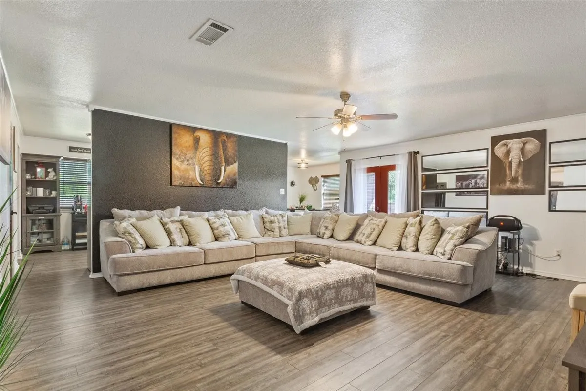 Living room with ceiling fan, a textured ceiling, dark wood-style flooring, and healthy amount of natural light