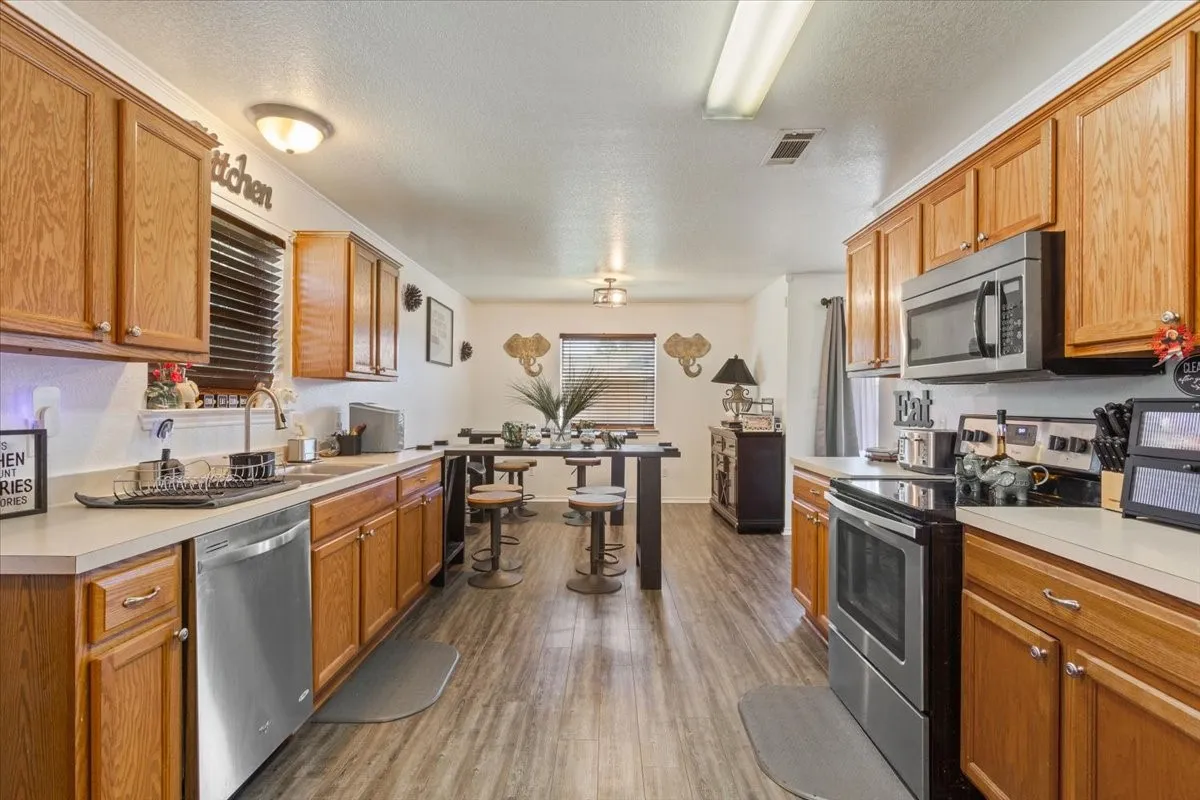 Kitchen with stainless steel appliances, light countertops, dark wood-type flooring, a textured ceiling, and wood finish cabinetry