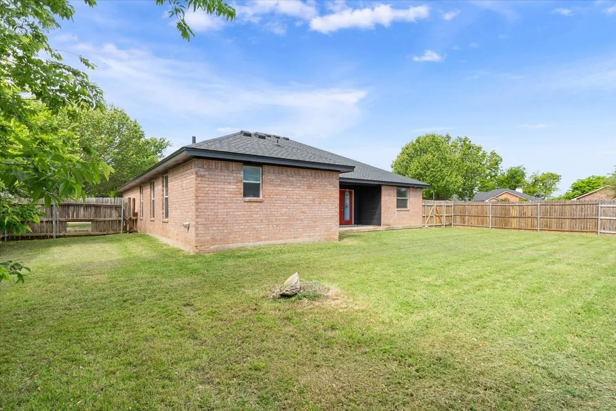 Rear view of house with a patio, a fenced backyard, brick siding, and roof with shingles