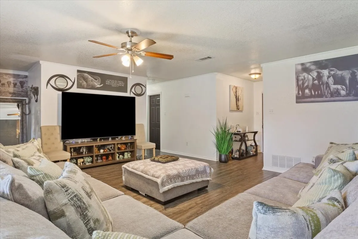 Living room with a textured ceiling, a ceiling fan, and wood finished floors