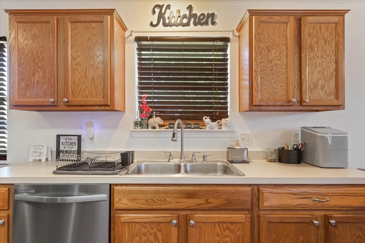 Kitchen with stainless steel dishwasher, light countertops, wood finish cabinets, and a textured wall