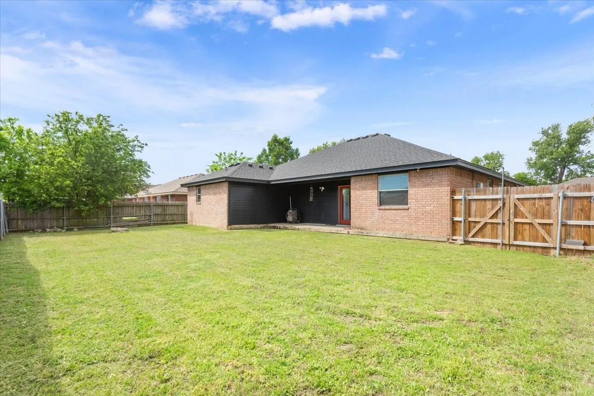 Rear view of house with a patio, brick siding, a fenced backyard, a gate, and roof with shingles
