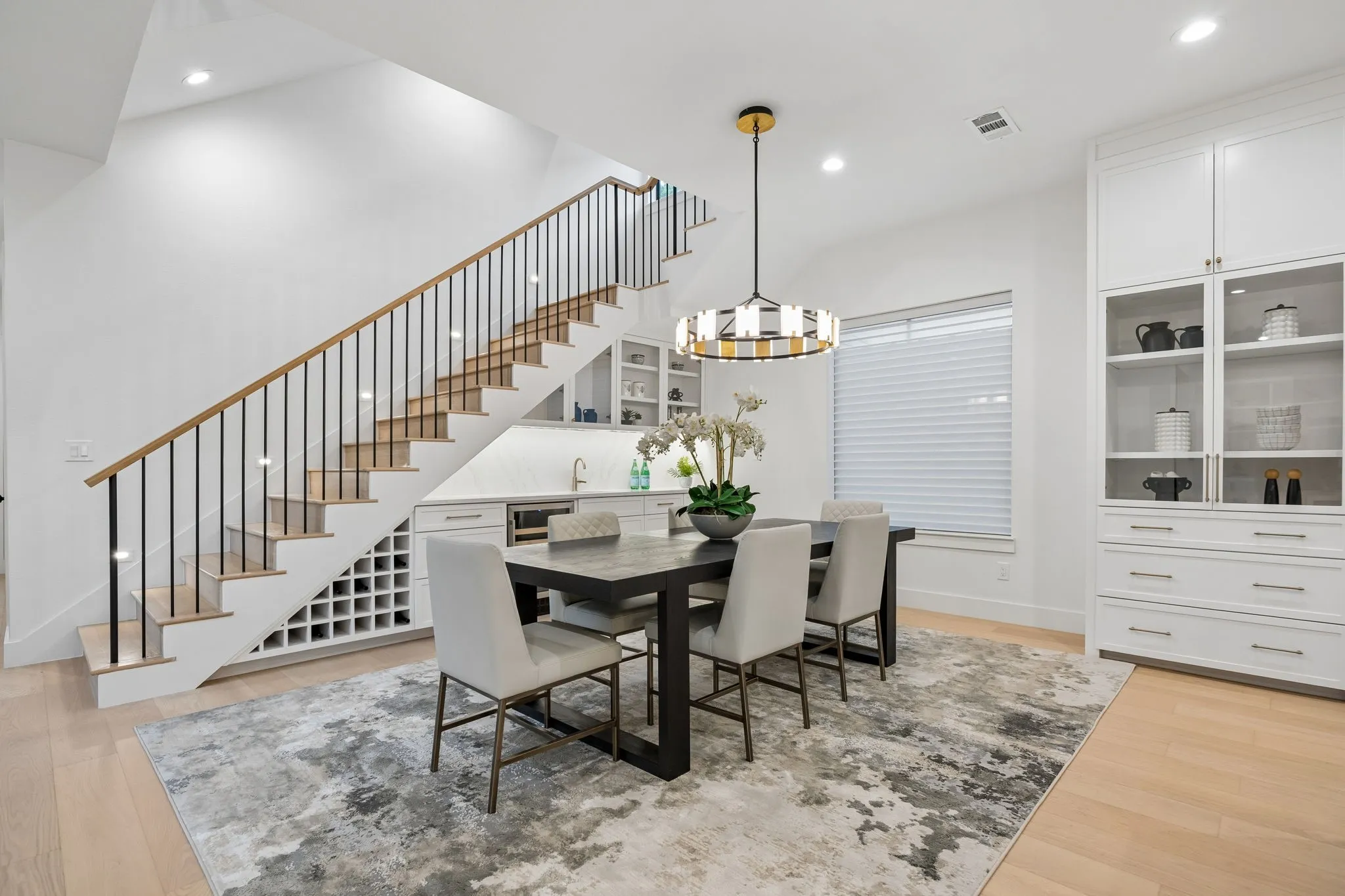 Dining area with designer lighting and built-in bar featuring wine storage and beverage fridge, conveniently tucked beneath the staircase.