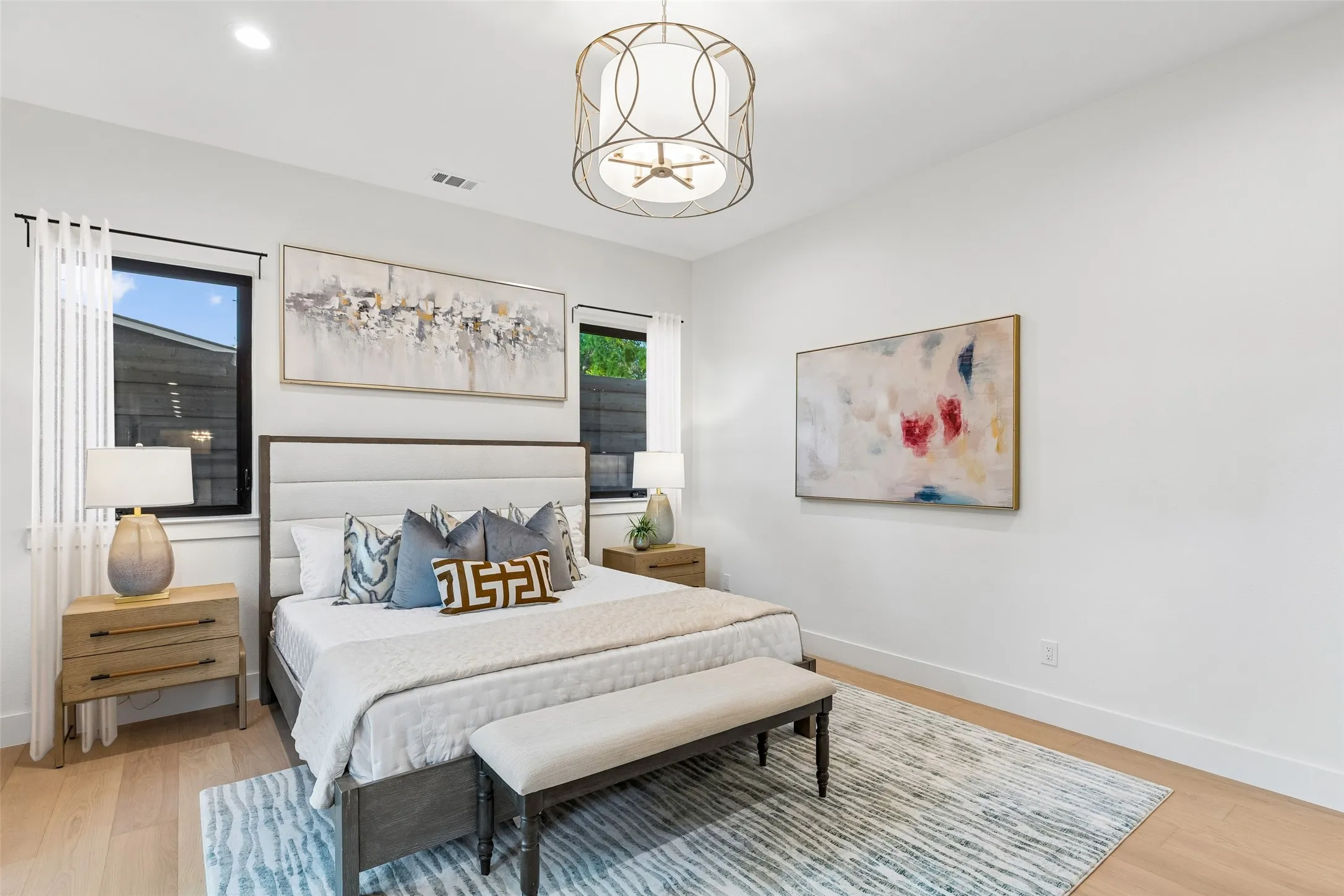 Spacious primary suite with designer lighting, warm wood floors, and serene views of the backyard.