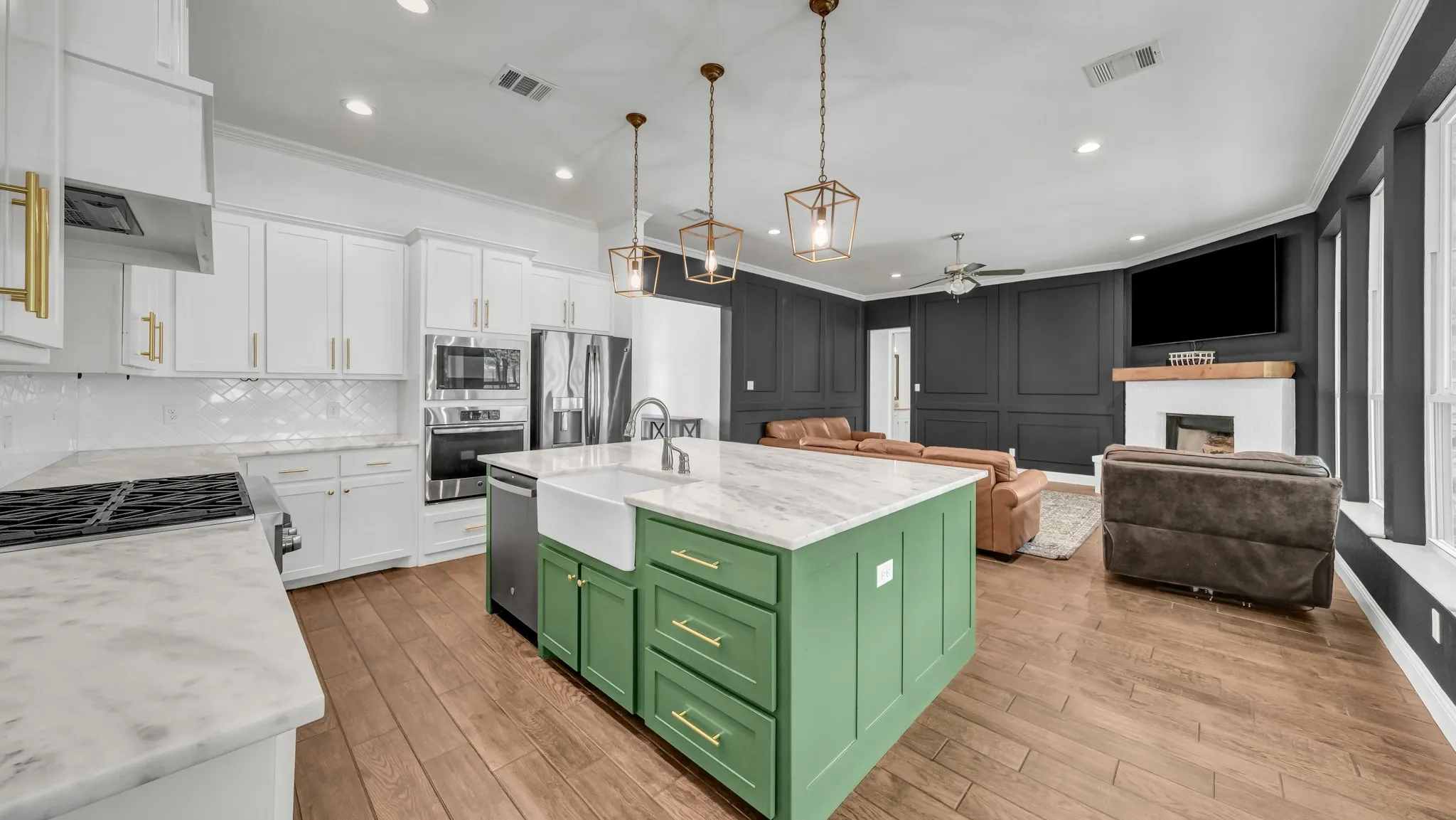 Dual tone kitchen featuring crown molding, open floor plan, an island with sink, a fireplace, and a ceiling fan